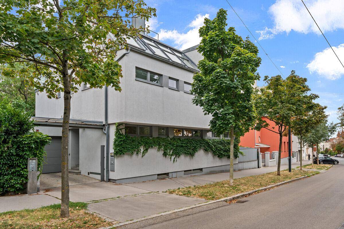 Moderne Hausfassade mit großen Fenstern, begrünten Wänden und Garage an einer ruhigen Straße.