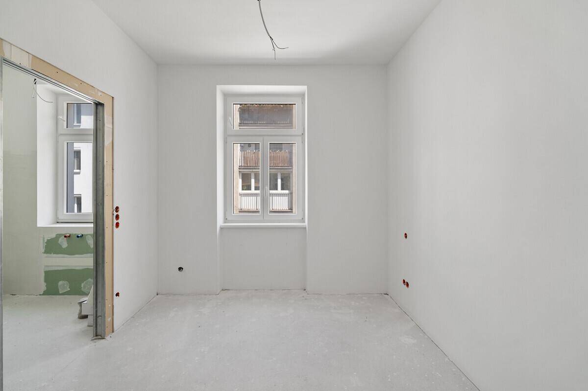 Zimmer im Rohbau mit Fenster und offenem Durchgang, bereit für den weiteren Ausbau.