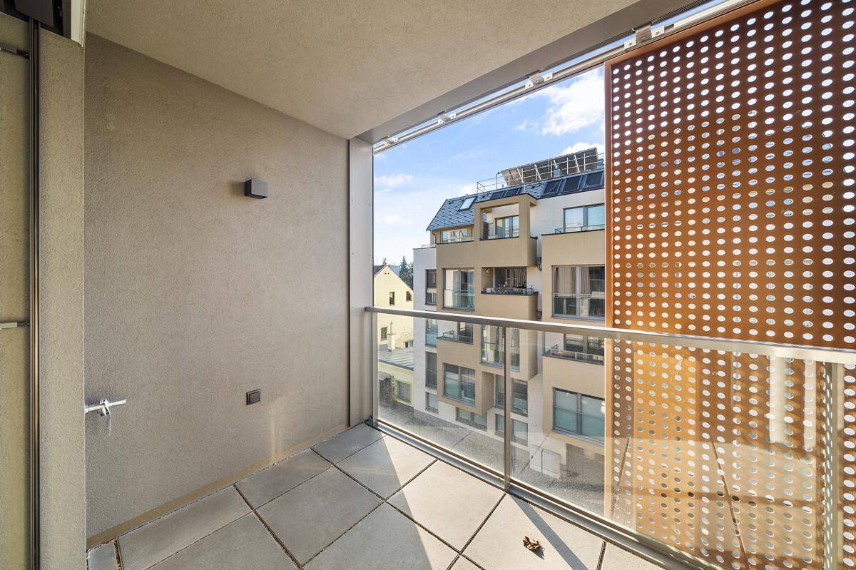 Heller Balkon mit Glasgeländer und perforierten Sichtschutzwänden, bietet Blick auf umliegende Gebäude.