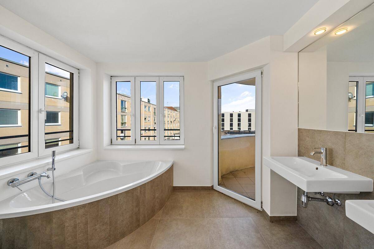 Modernes Badezimmer mit Badewanne, Fliesenboden und Zugang zu einem kleinen Balkon.