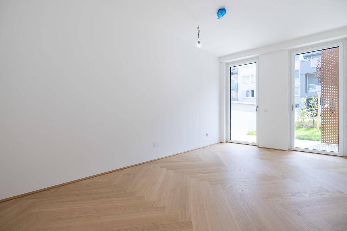 Heller, leerer Raum mit elegantem Fischgrätparkett und großen Fenstern zum Außenbereich.