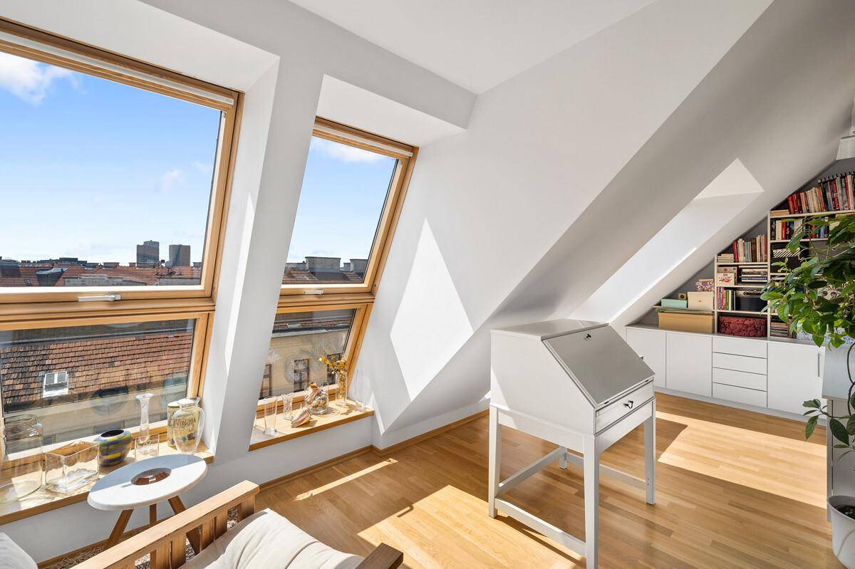 Helles Dachgeschosszimmer mit schrägen Wänden, Dachfenstern und Blick über die Stadt.