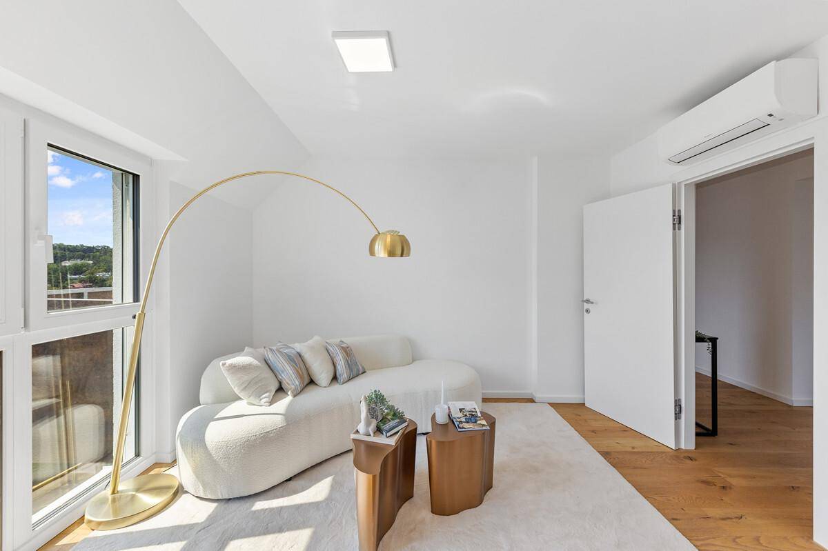 Gemütliches Wohnzimmer mit hellem Sofa, Holzboden und großen Fenstern für viel Tageslicht.