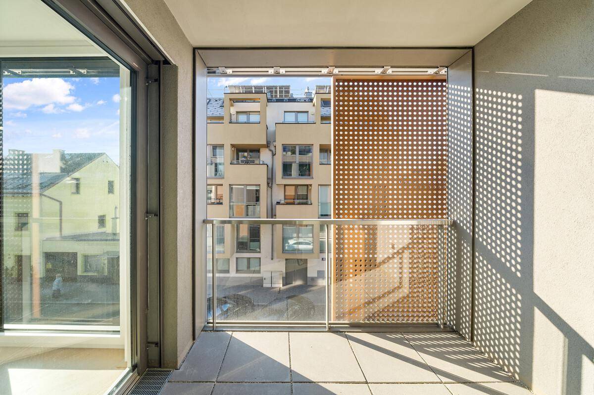 Moderner Balkon mit Fliesenboden, Glasgeländer und perforiertem Holz-Sichtschutz.