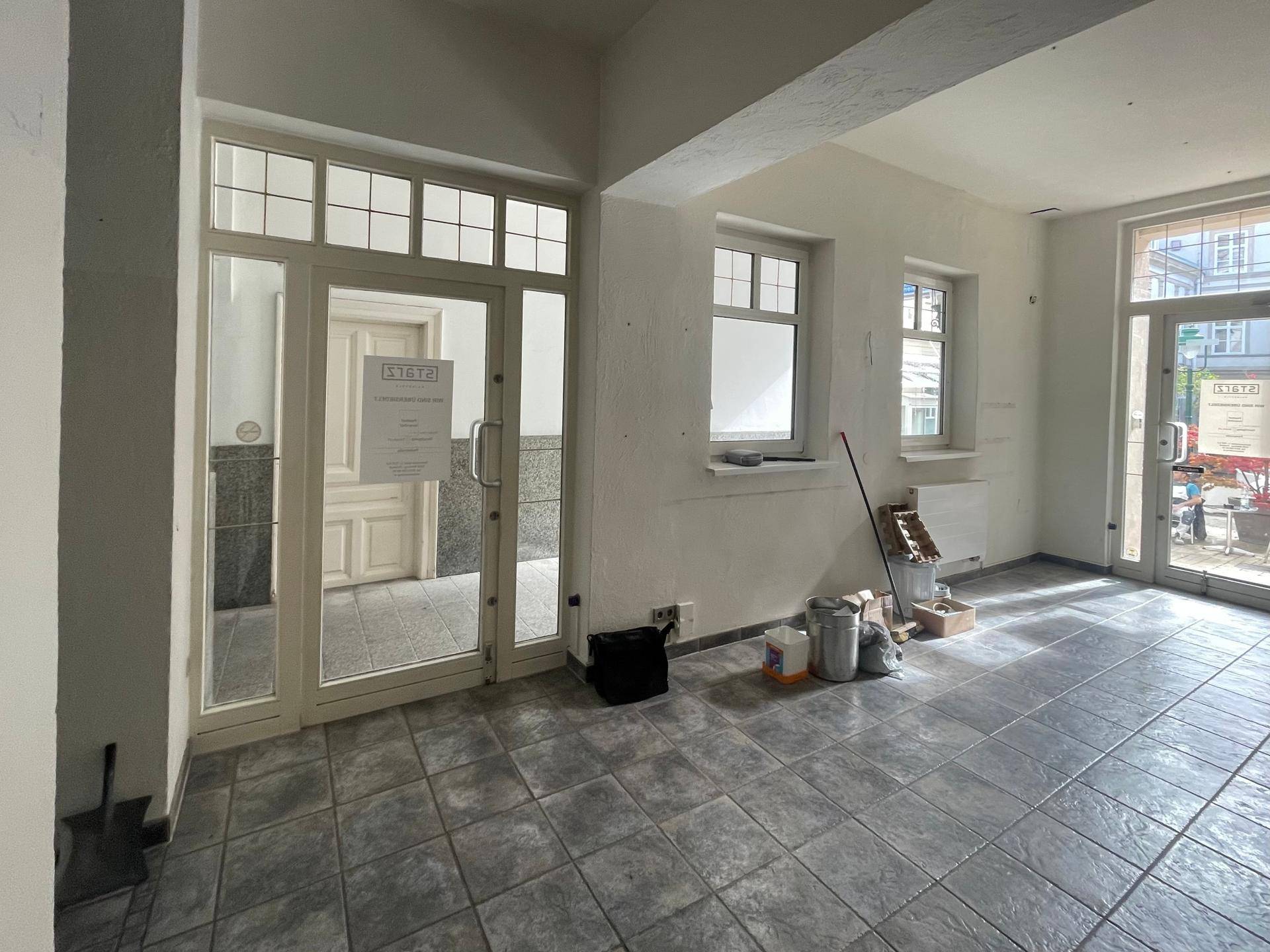 Eingangsbereich eines Gewerberaums mit großen Glastüren und Fliesenboden, der zum Innenhof führt.