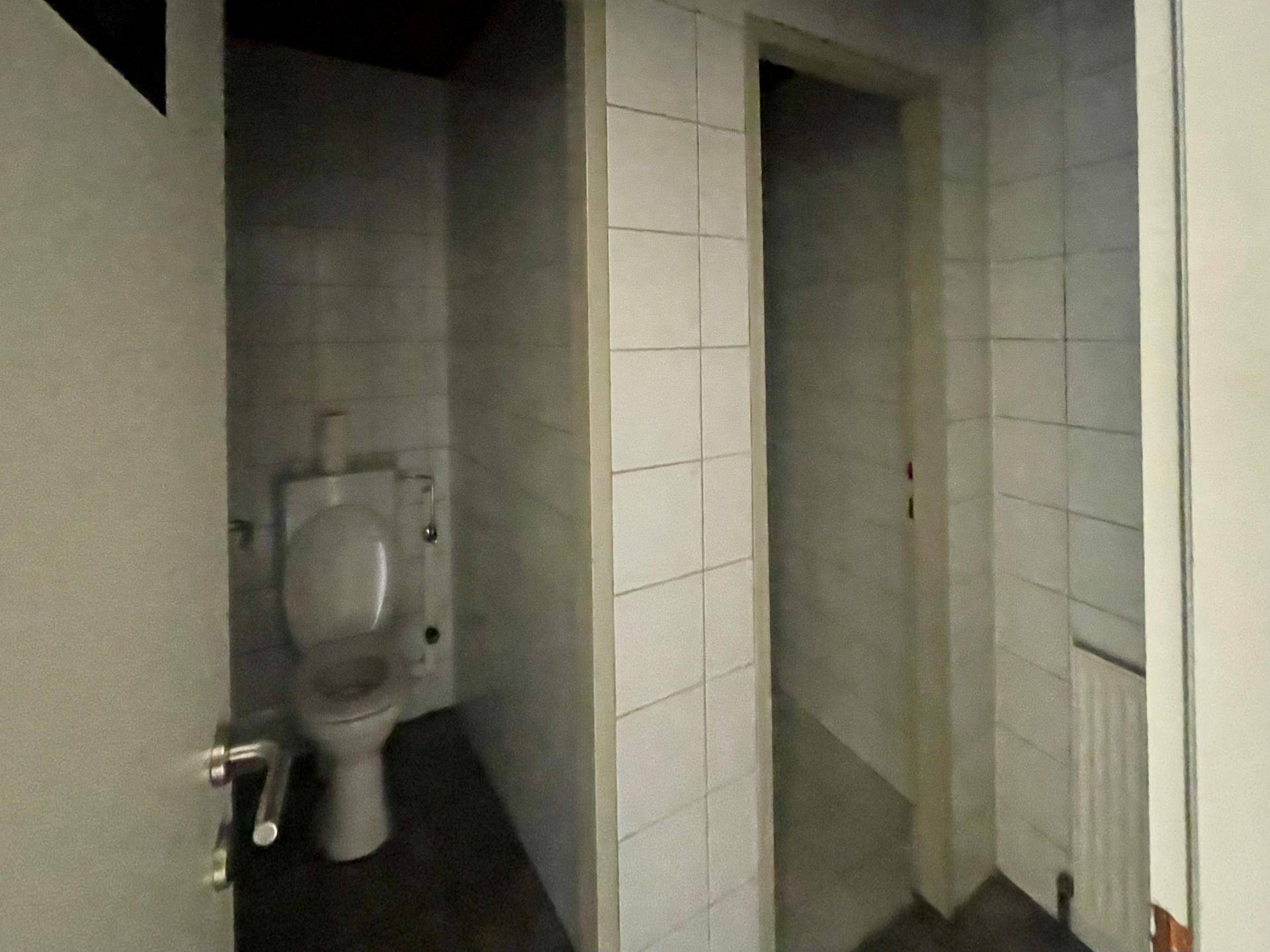 Einfache Toilette mit weißen Fliesen und Standardausstattung, funktional und sauber.