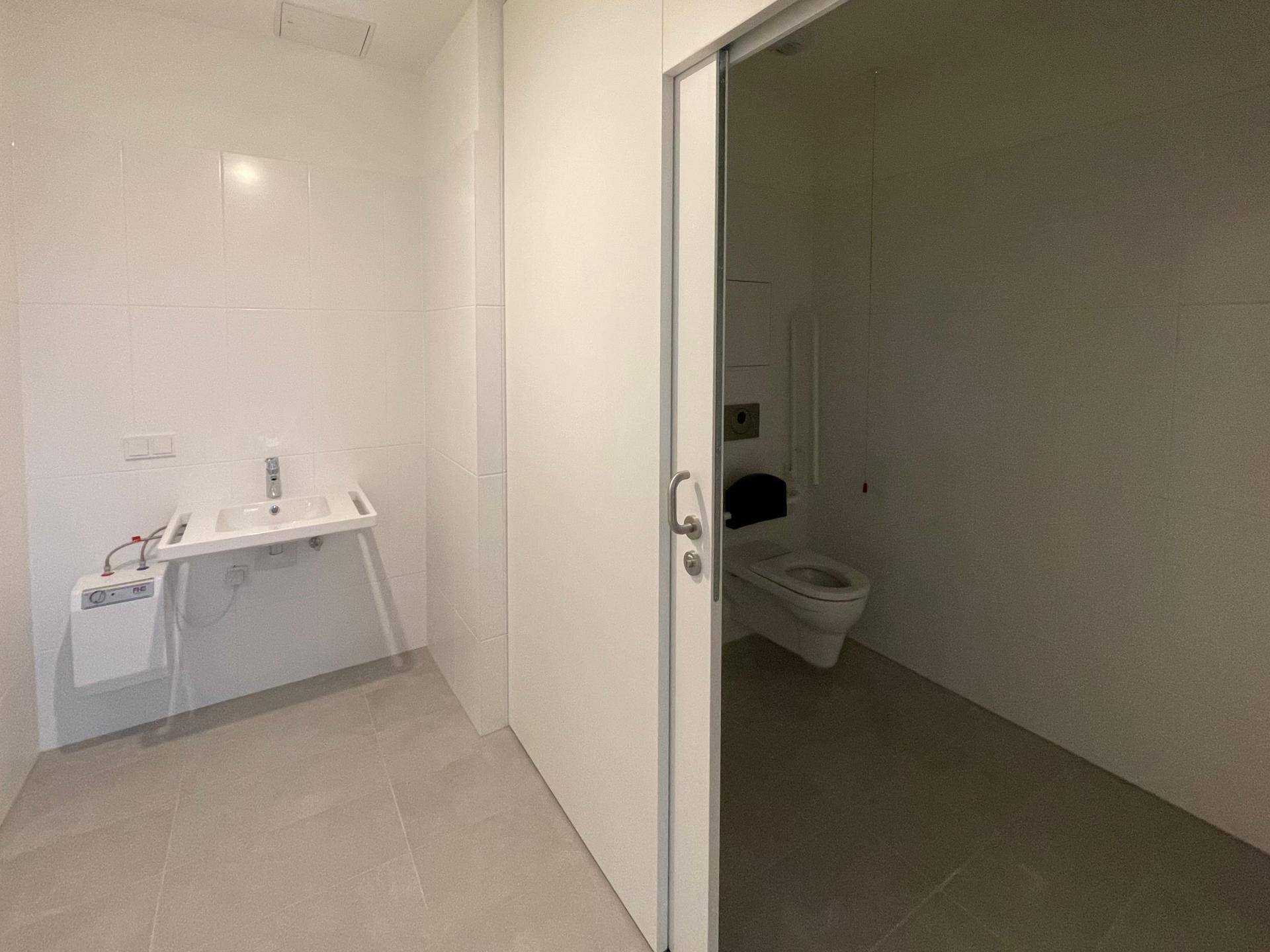 Barrierefreies Badezimmer mit Waschbecken, Toilette und Haltegriffen, ausgestattet mit hellen Fliesen.