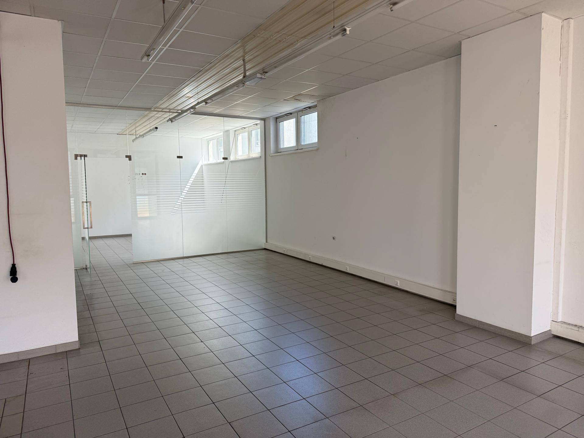 Heller Gewerberaum mit Fliesenboden, weißen Wänden und einer Glasabtrennung im Hintergrund.