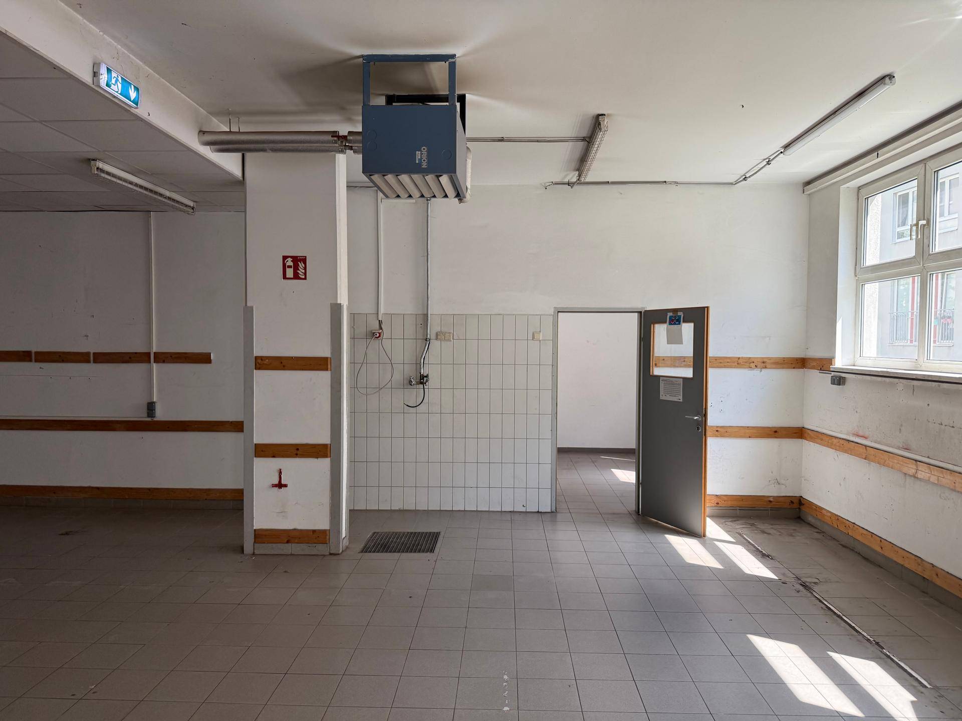 Nutzraum mit gefliestem Bereich, Fenster und einer Duschvorrichtung an der Wand.