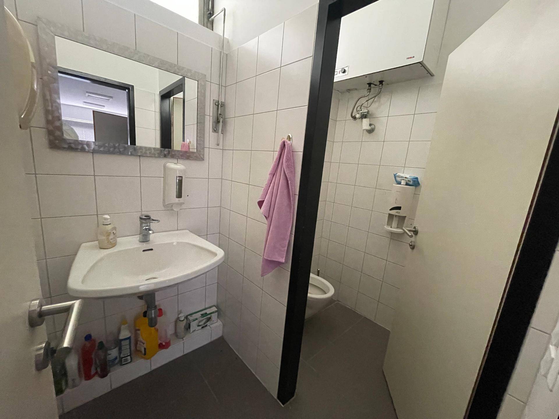 Kleiner Toilettenraum mit Waschbecken, Spiegel und weißen Wandfliesen, ausgestattet mit einem Abluftventilator.