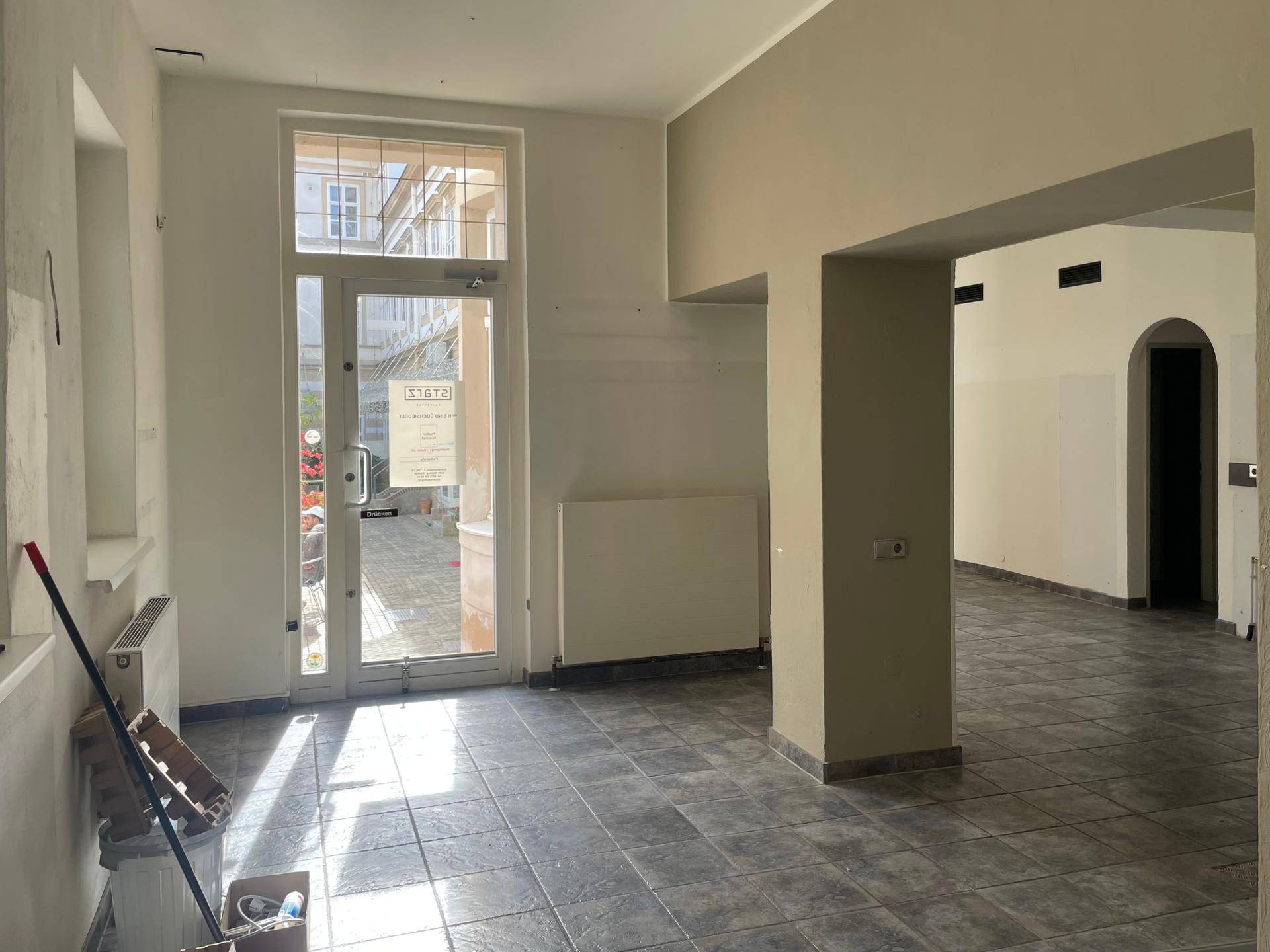 Geräumiger Gewerberaum mit Fliesenboden, großen Fenstern und viel Tageslicht, bereit für den Ausbau.