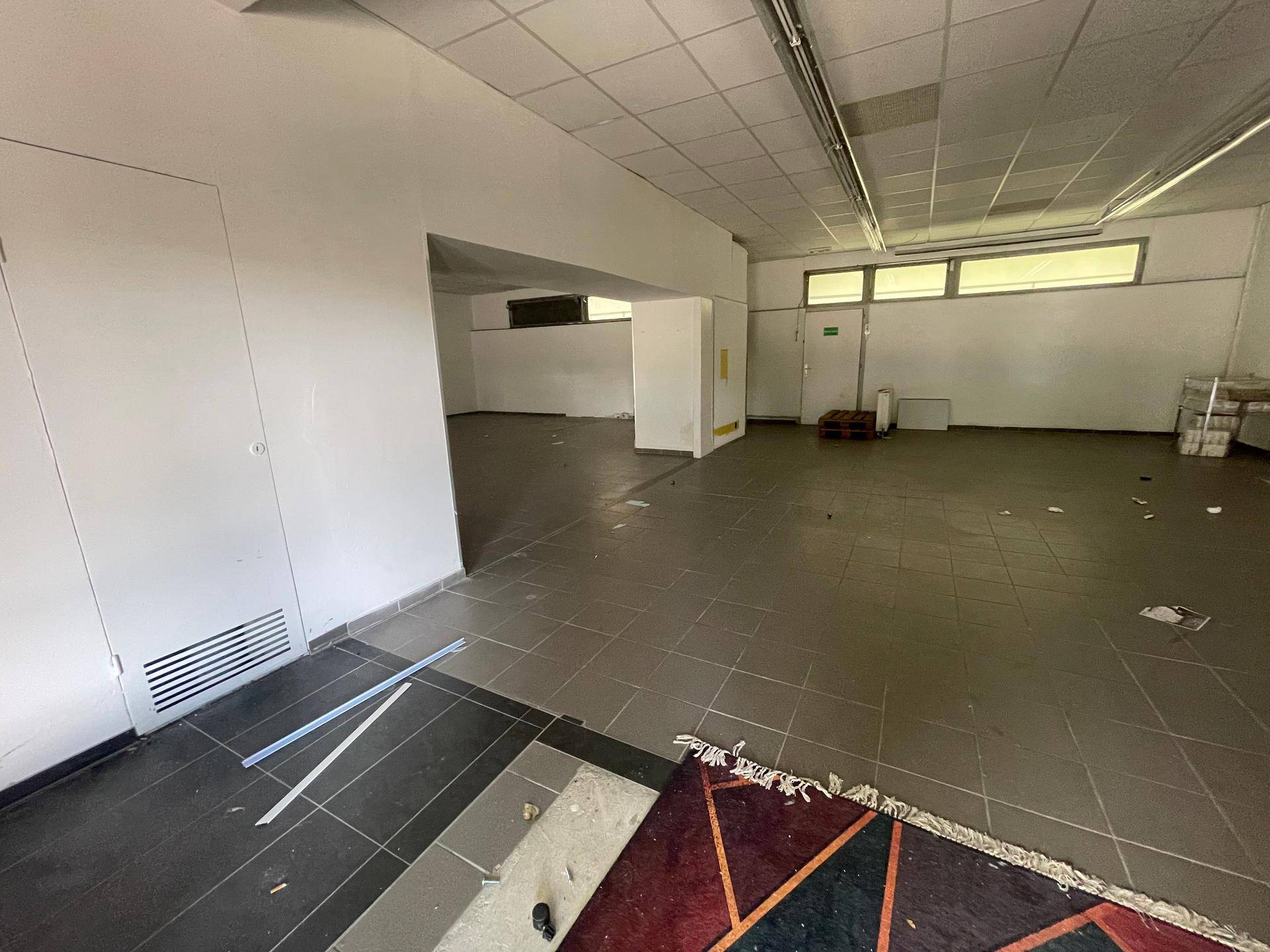 Großer, leerstehender Gewerberaum mit Fliesenboden und Fenstern im oberen Bereich der Wand.