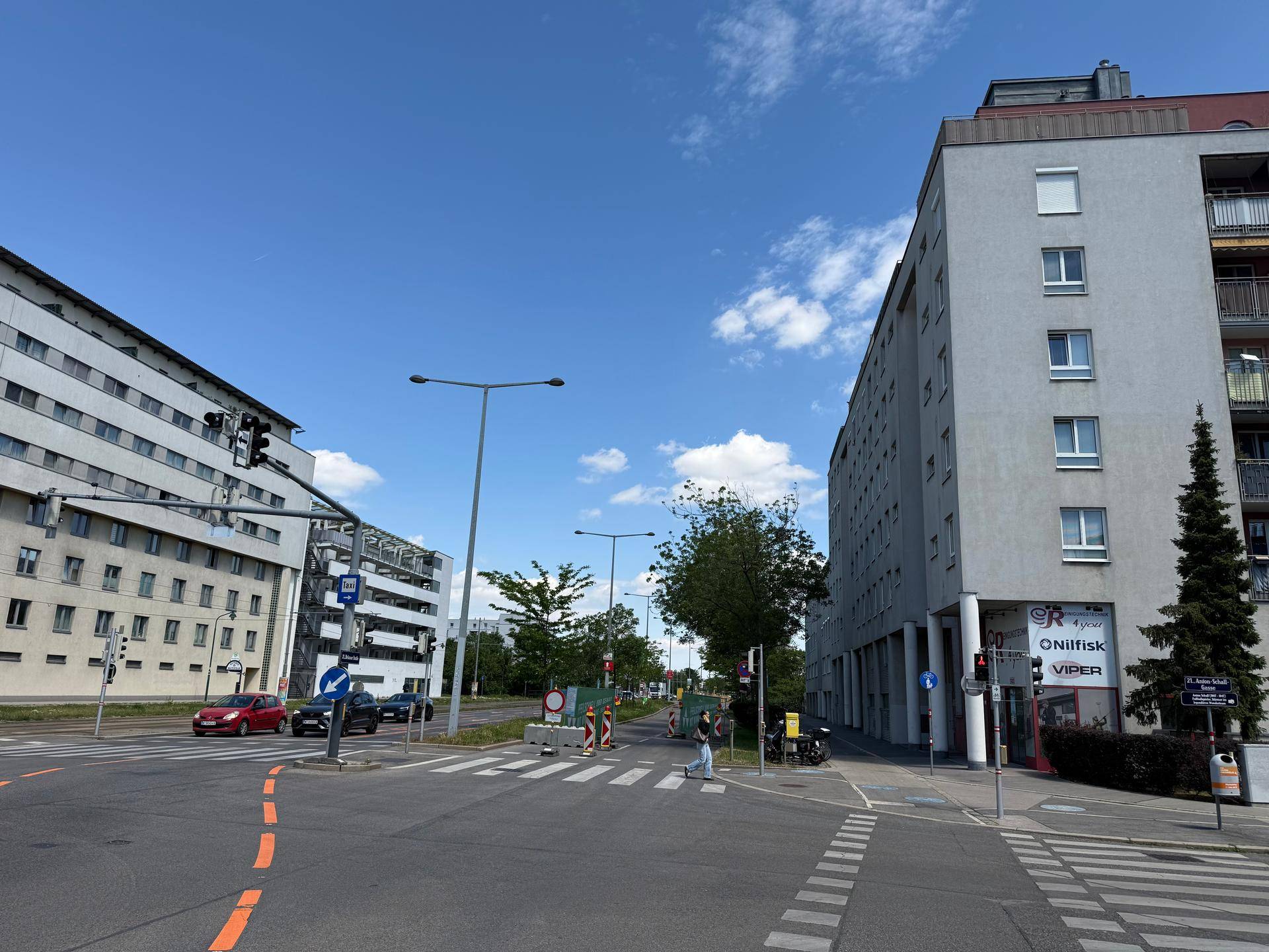 Weitwinkelaufnahme einer städtischen Kreuzung mit einem modernen Gebäude und umliegender Infrastruktur.