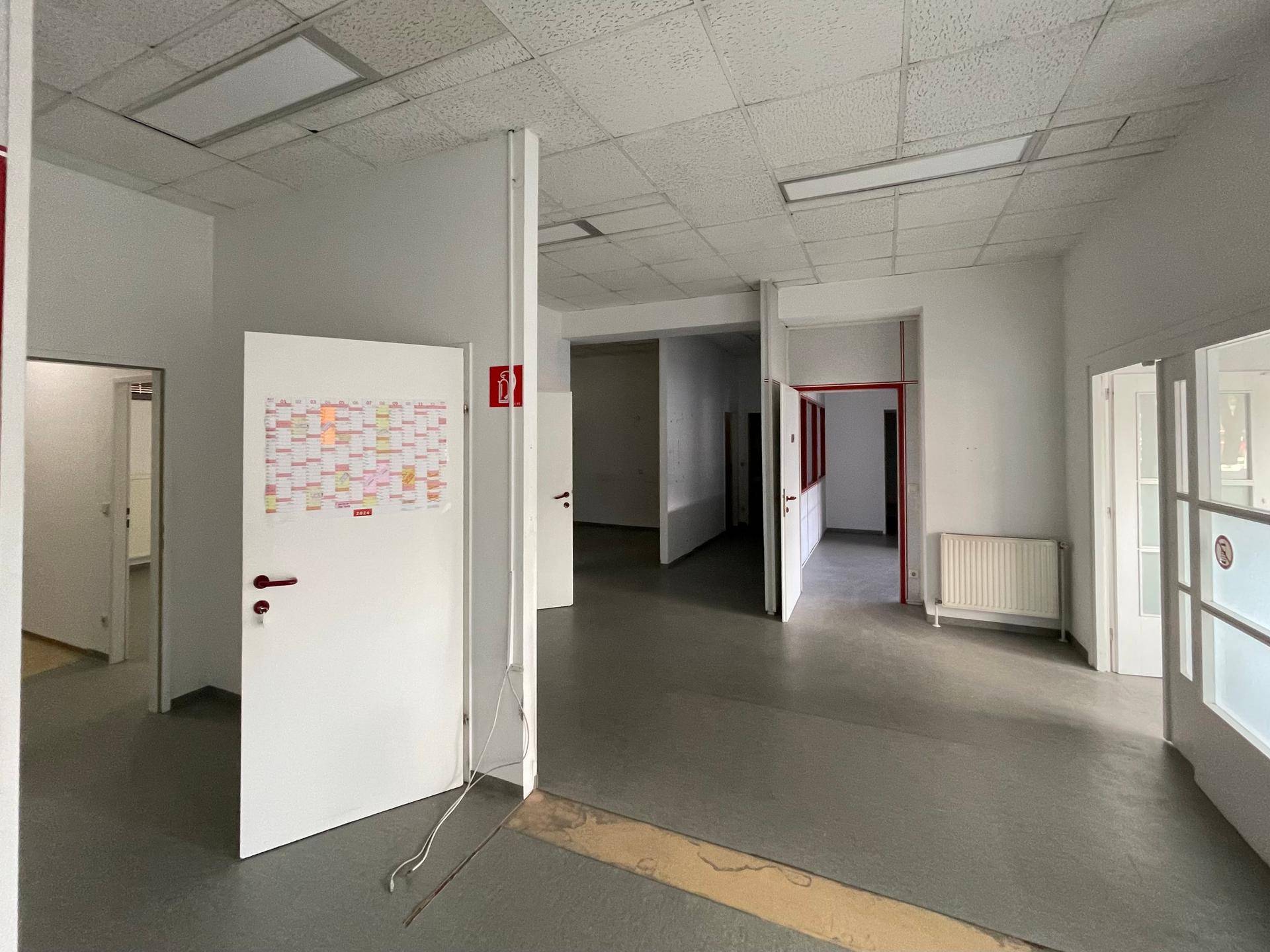 Geräumiger, leerstehender Gewerberaum mit mehreren Türen und einem funktionalen Bodenbelag.
