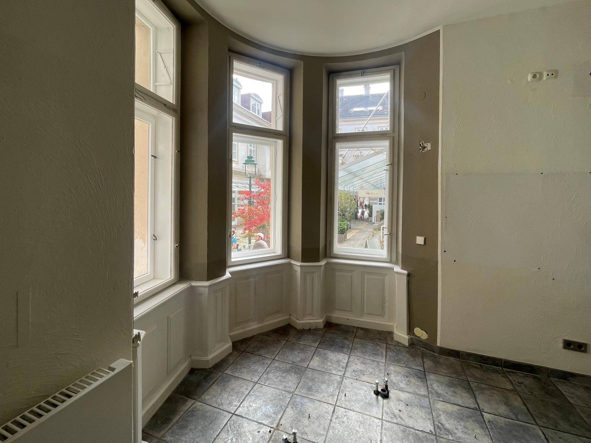 Heller Gewerberaum mit Erkerfenstern, die einen Blick auf den belebten Innenhof bieten.