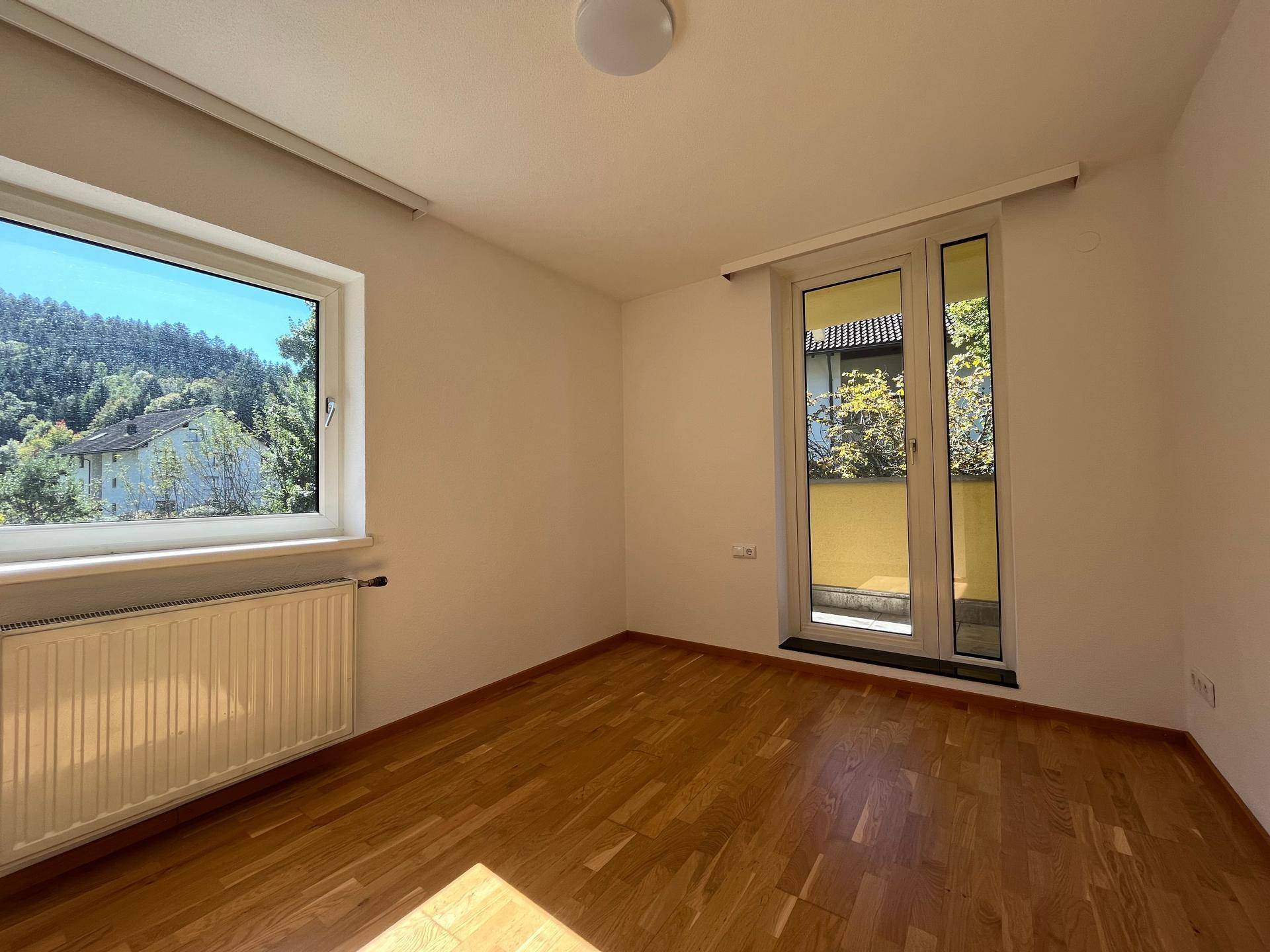 Schlafzimmer mit Holzboden und großem Fenster, das einen Blick ins Grüne bietet.