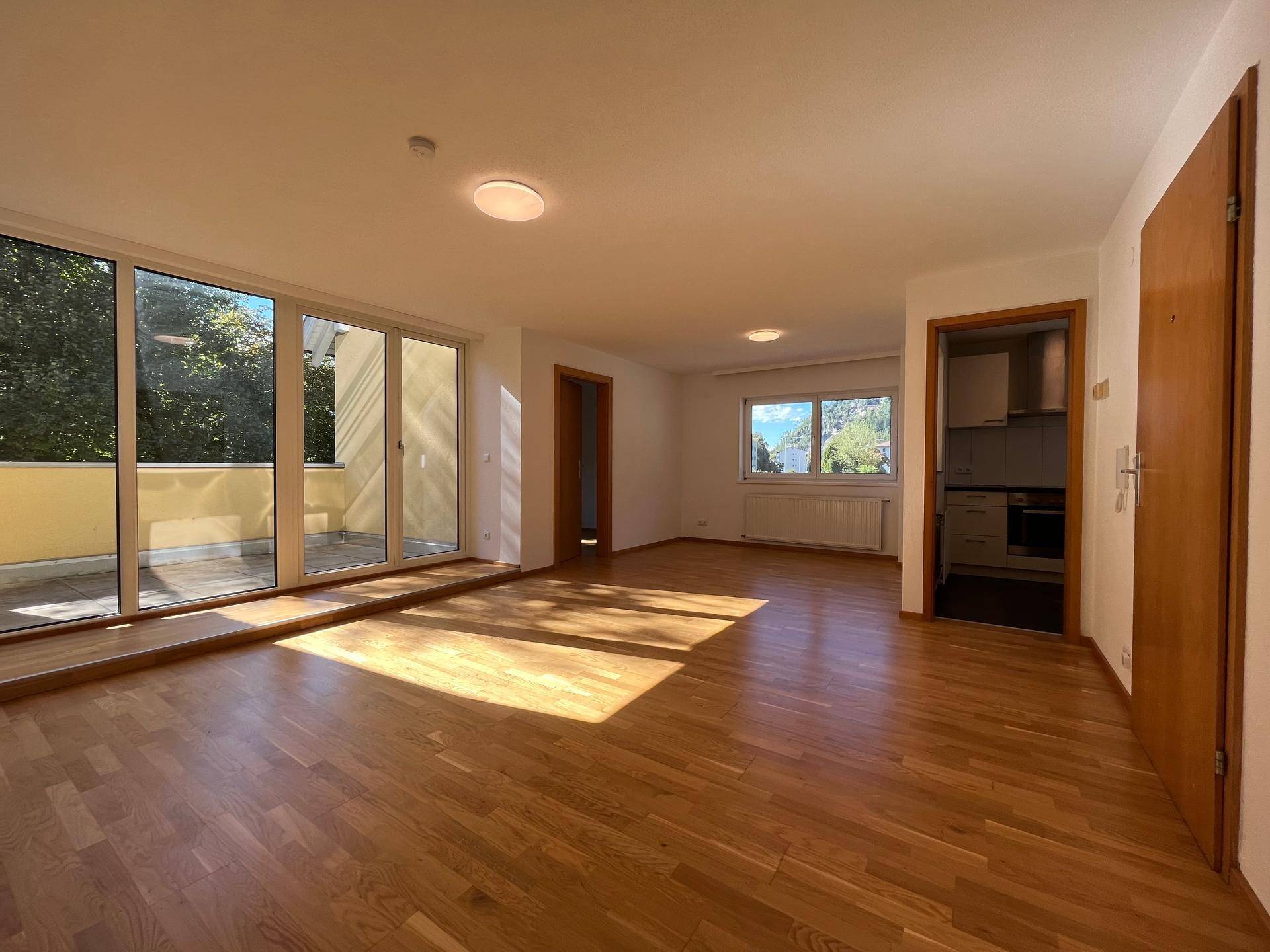 Geräumiges Wohnzimmer mit Holzboden, großen Fenstern und Zugang zu einem Balkon, hell und einladend.