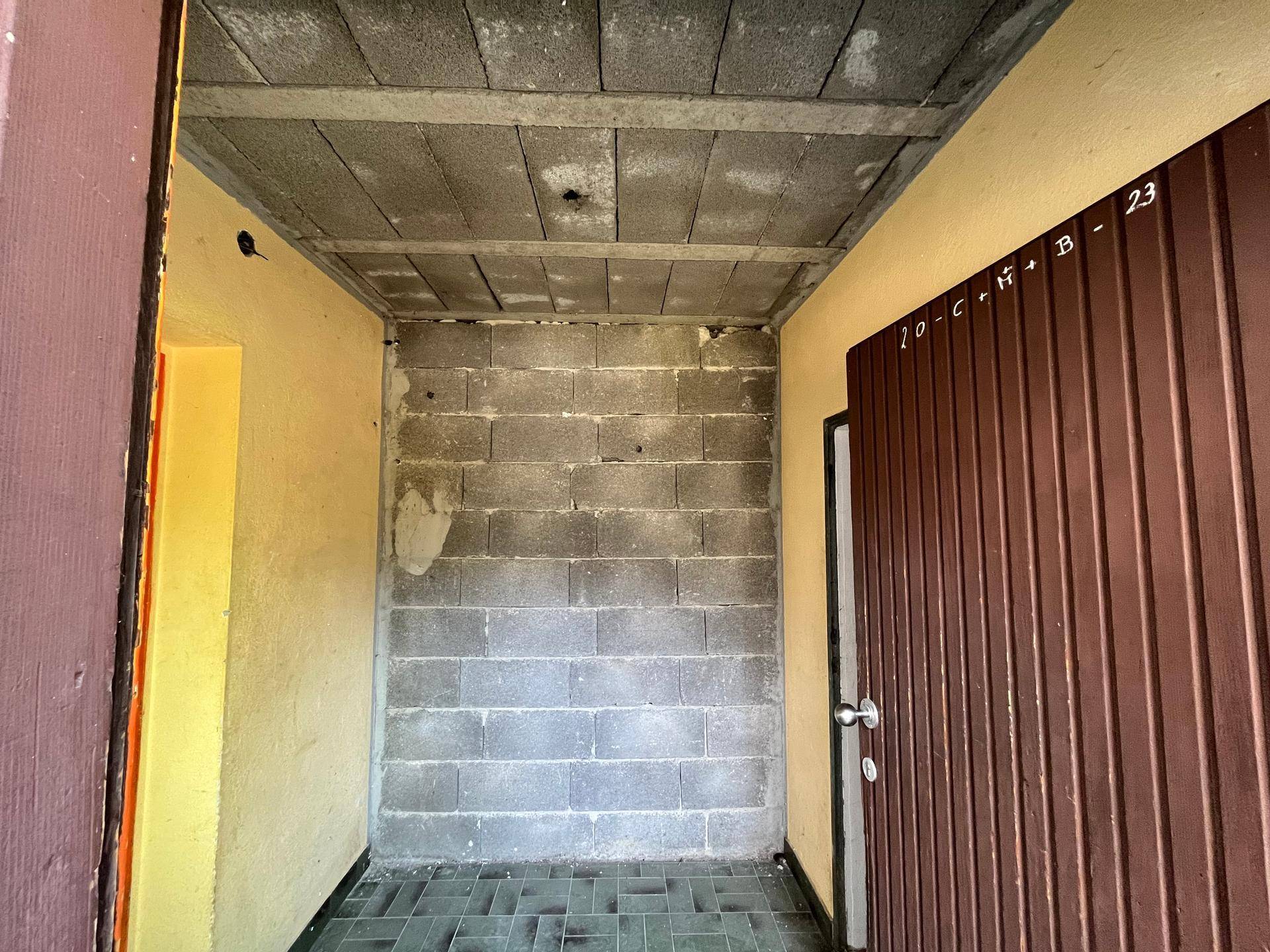 Eingangsbereich mit Fliesenboden und unverputzten Ziegelwänden, der zu einer Garage führt.
