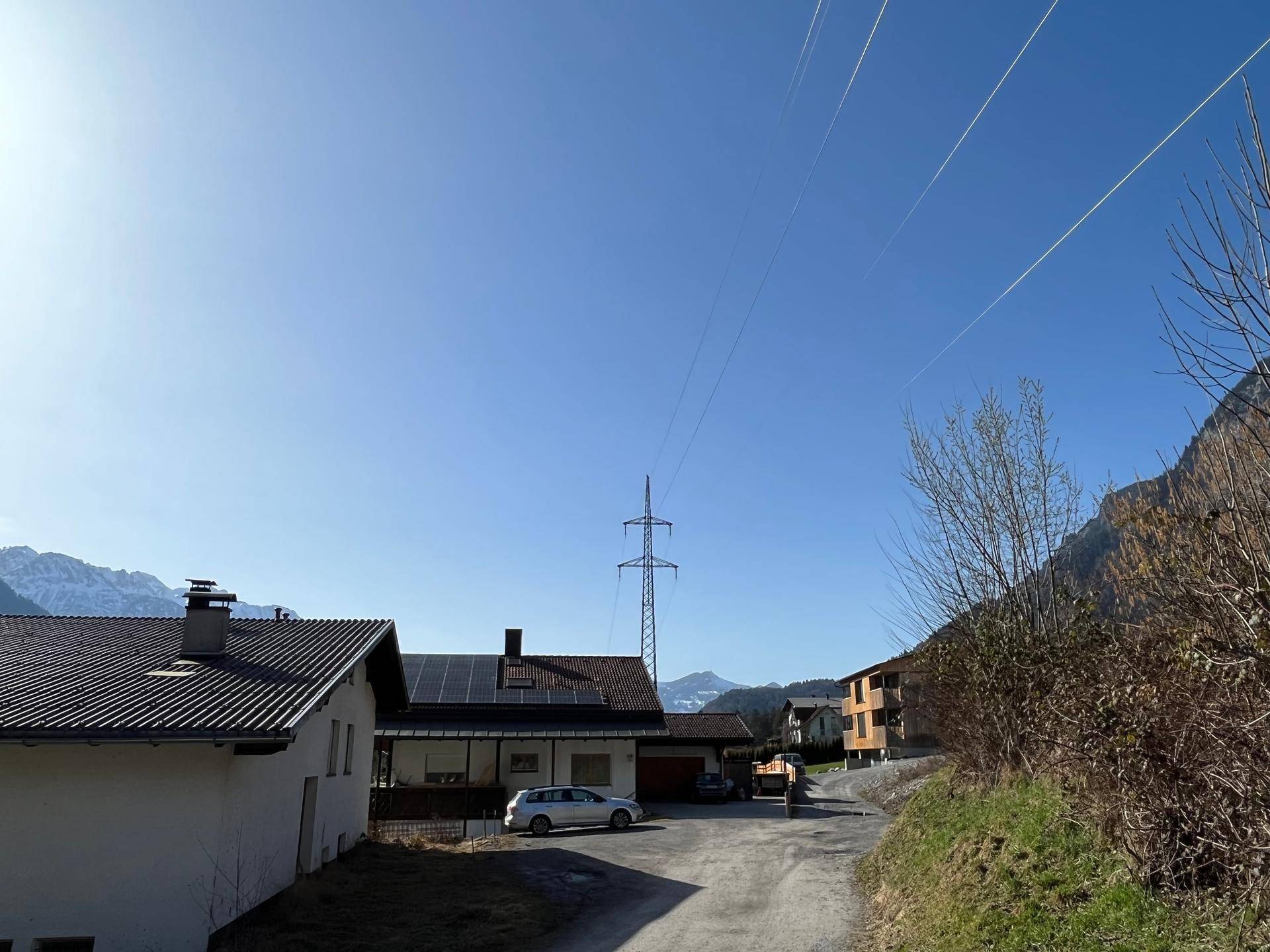Ländliche Straße mit benachbarten Häusern und Stromleitungen unter blauem Himmel.