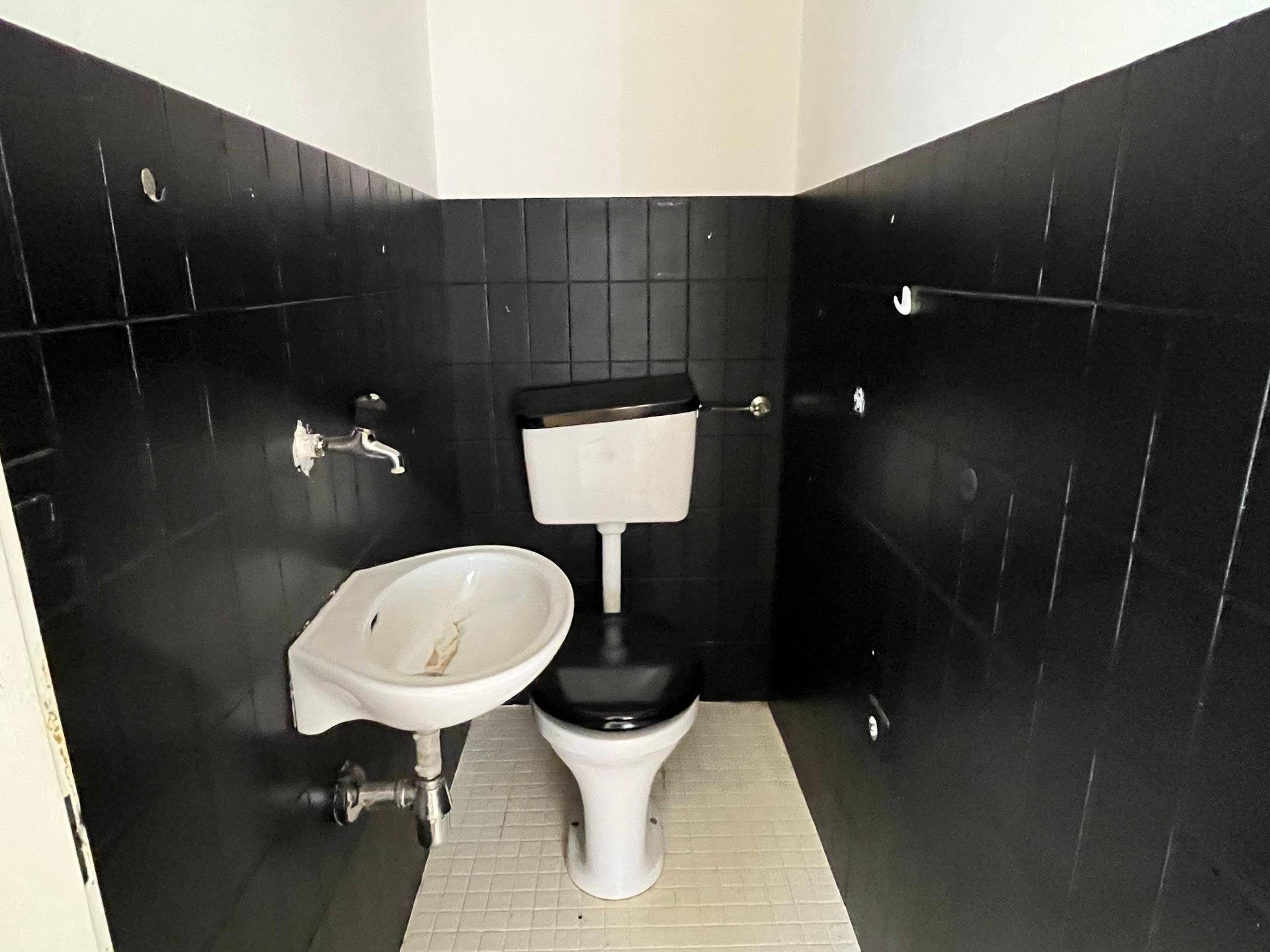 Kleines WC mit schwarzen Fliesen und weißer Keramik, das eine Modernisierung benötigt.
