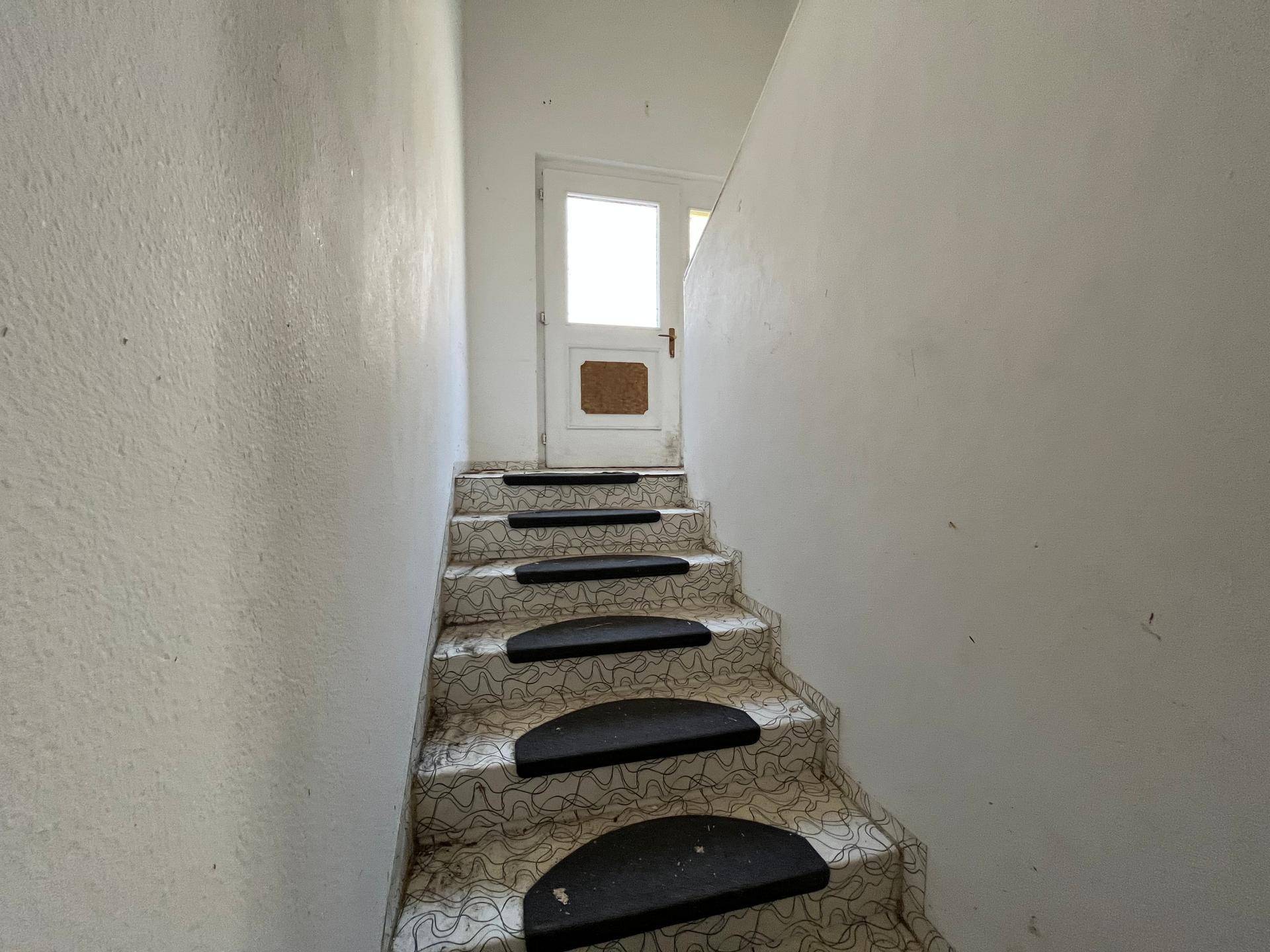 Treppenhaus mit gemustertem Bodenbelag und weiß gestrichenen Wänden, das in die obere Etage führt.