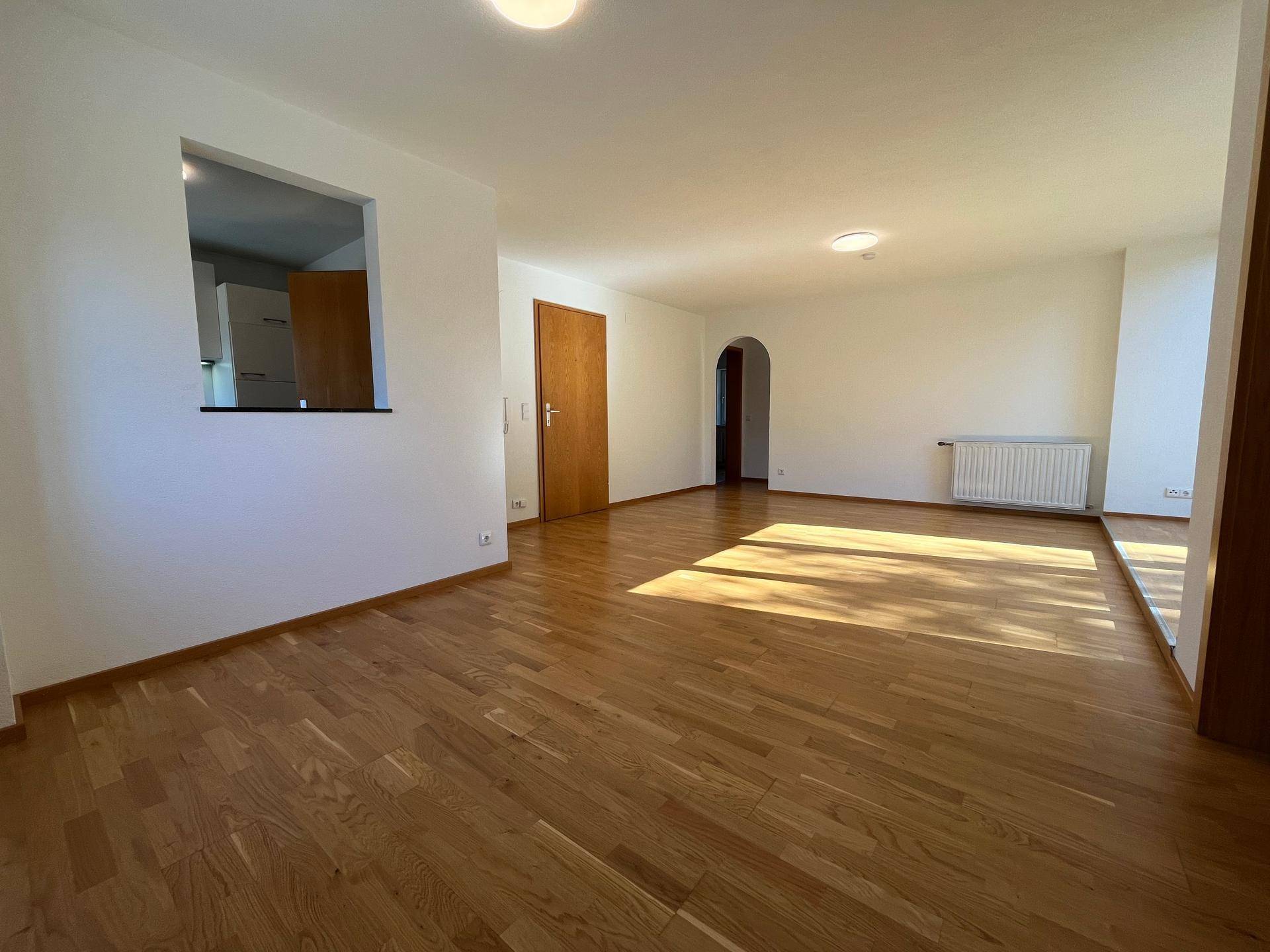 Offener Wohnbereich mit Holzboden und Durchgang zur Küche, hell und freundlich.