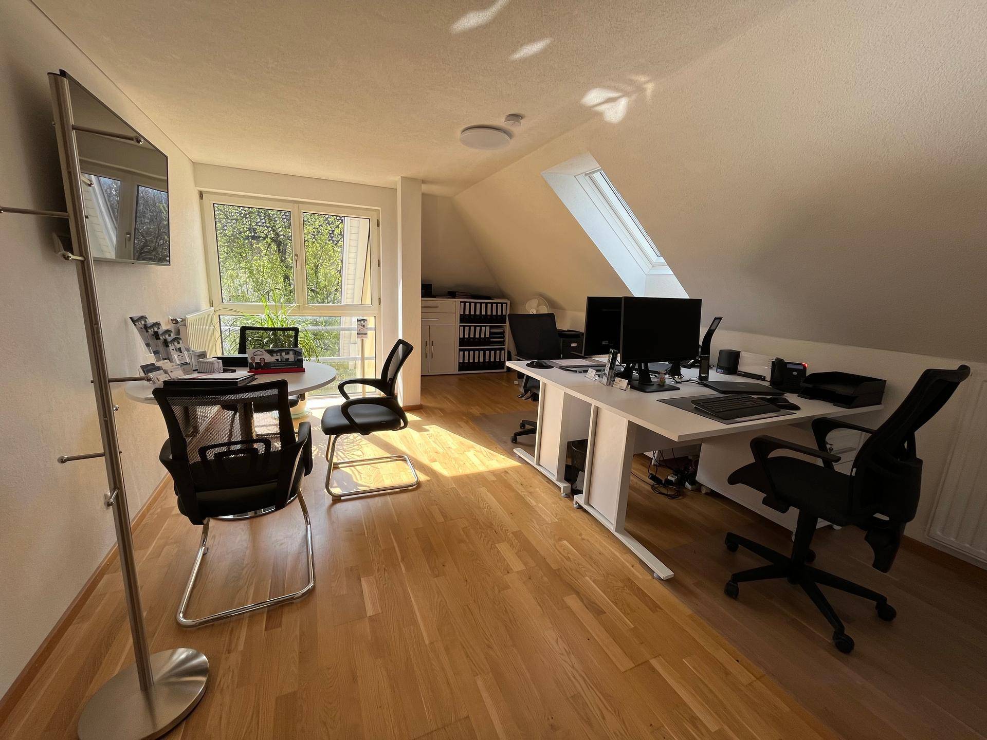 Helles Büro im Dachgeschoss mit mehreren Arbeitsplätzen und Holzboden, gut beleuchtet.
