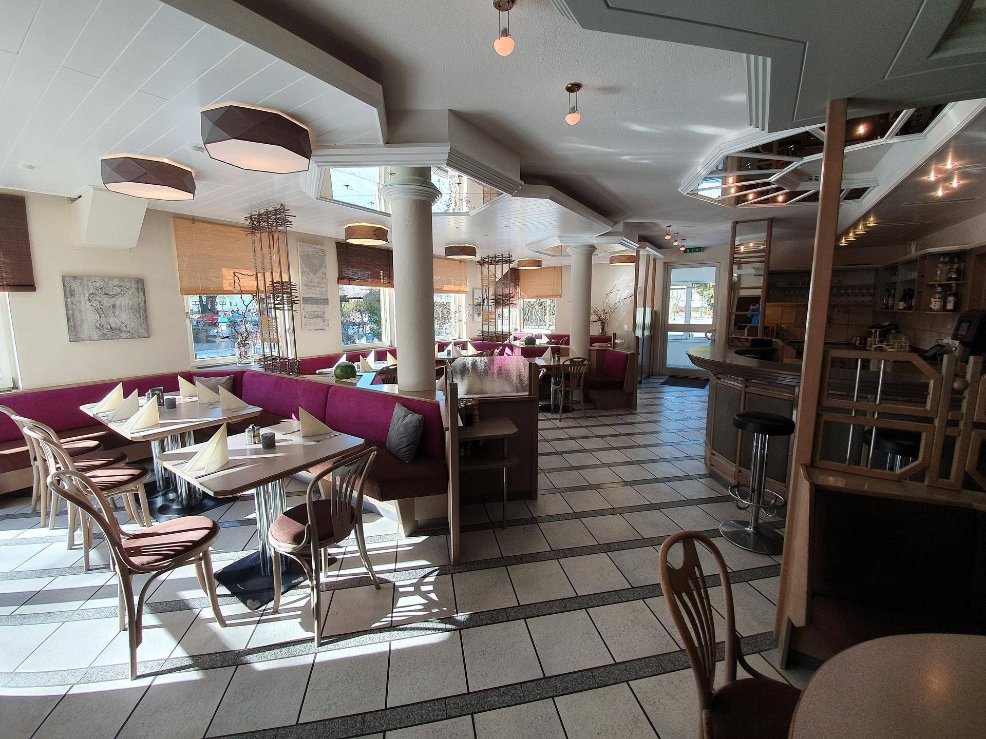 Heller und geräumiger Restaurantbereich mit verschiedenen Sitzgelegenheiten, Bar und Fliesenboden.