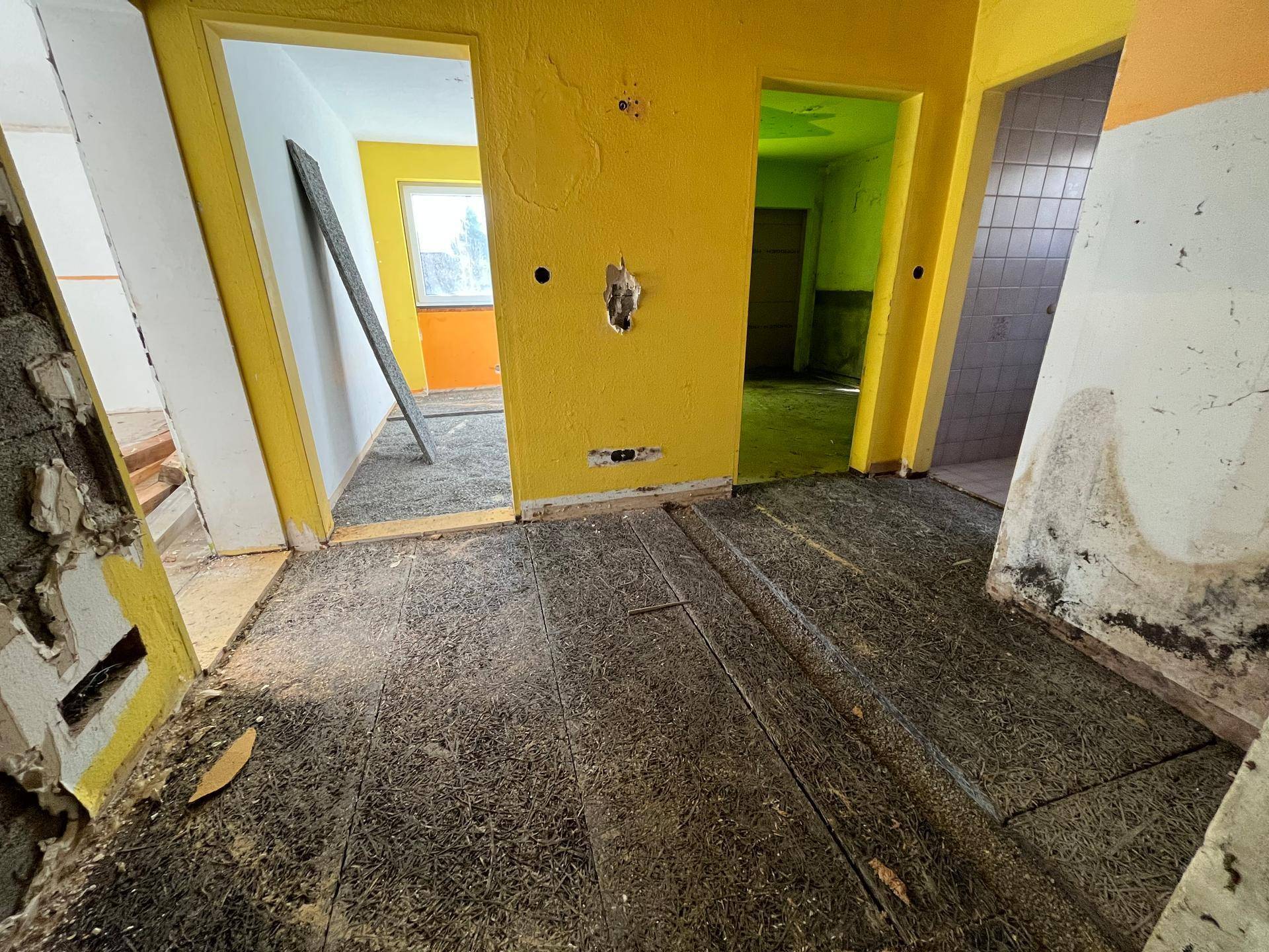 Innenraum mit mehreren Türöffnungen und beschädigtem Boden, der auf Renovierung wartet.