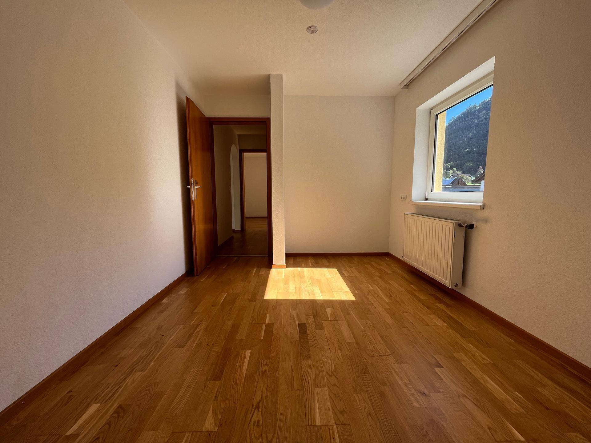 Schlafzimmer mit Holzboden und Fenster, das viel Tageslicht hereinlässt, schlicht und funktional.