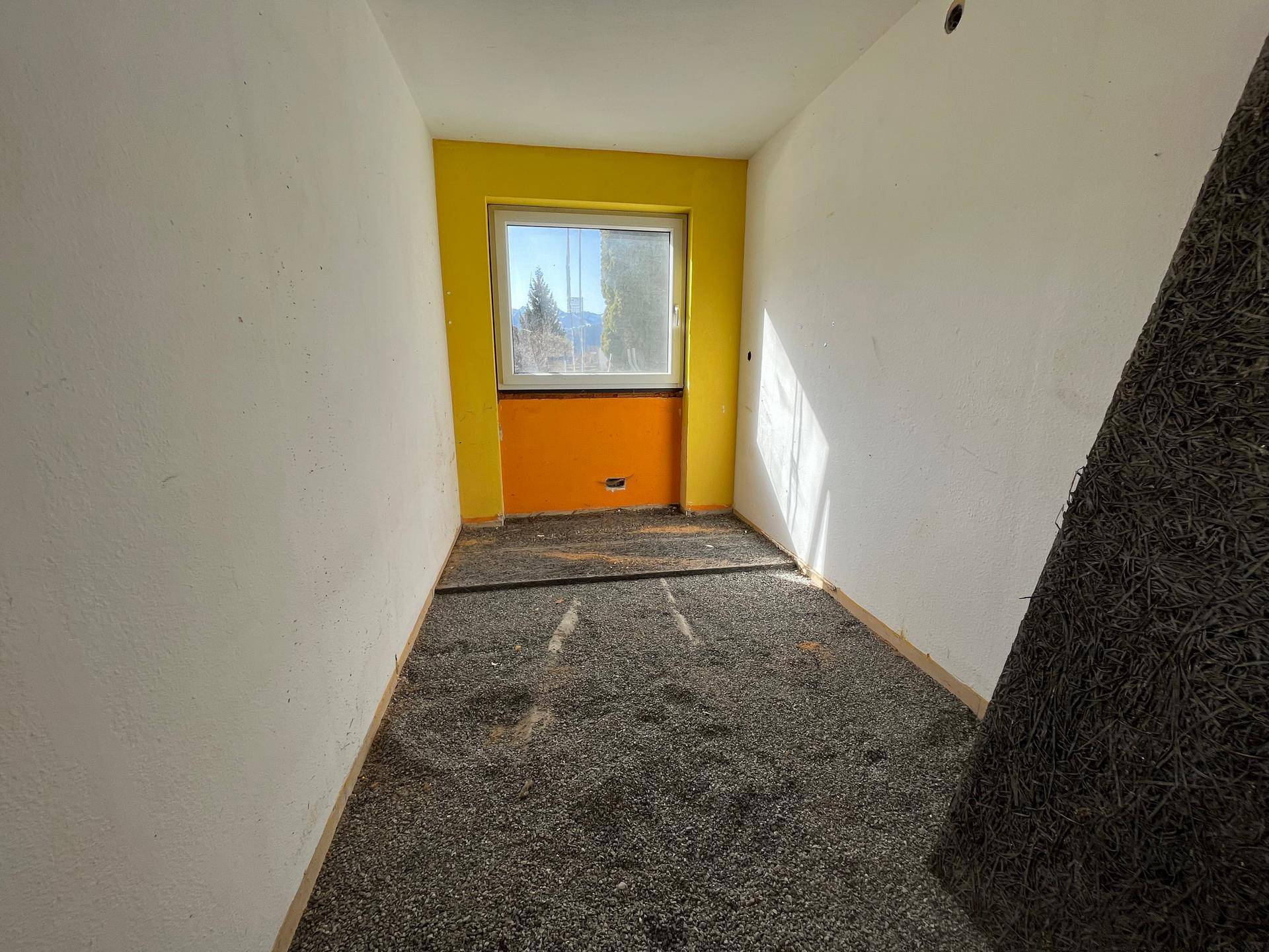 Kleiner Raum mit gelben und weißen Wänden, Fenster und vorbereitetem Boden für Renovierung.