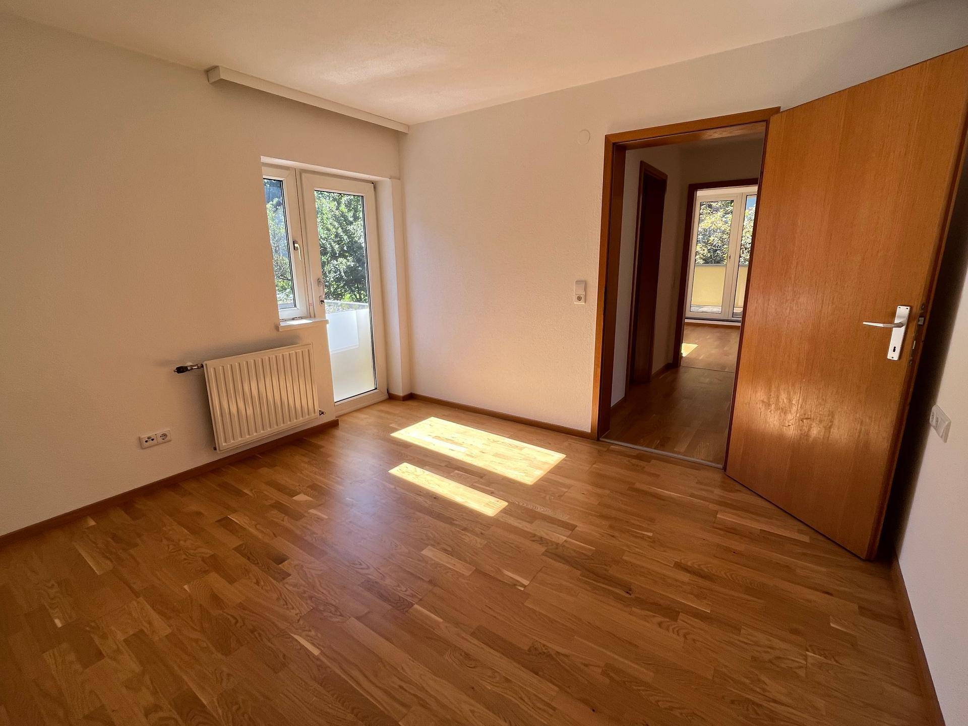 Helles Schlafzimmer mit Holzboden und Zugang zu einem Balkon, gut beleuchtet.
