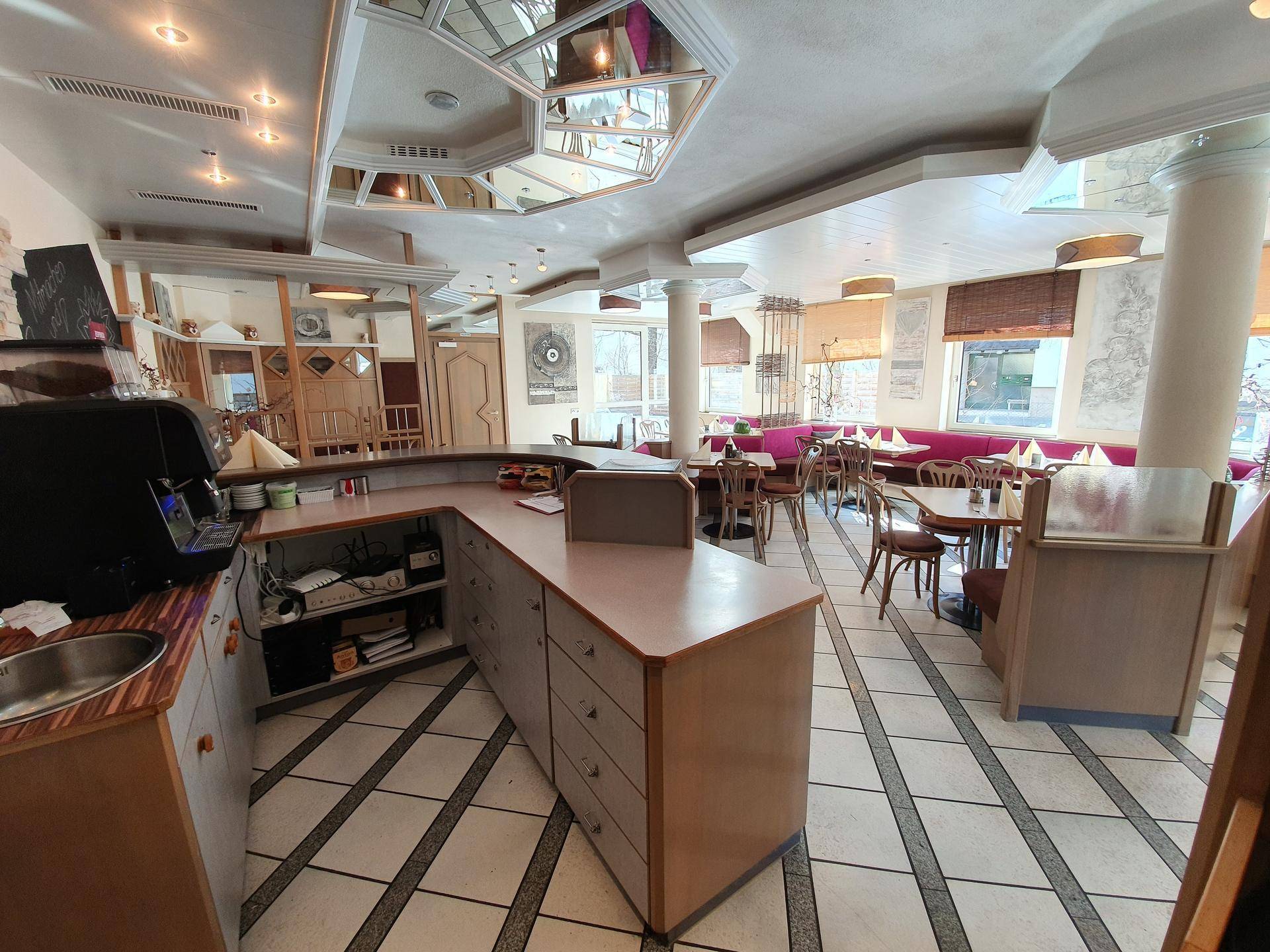 Restaurantinterieur mit Thekenbereich, Sitzgelegenheiten und dekorativen Elementen, durchflutet von Tageslicht.