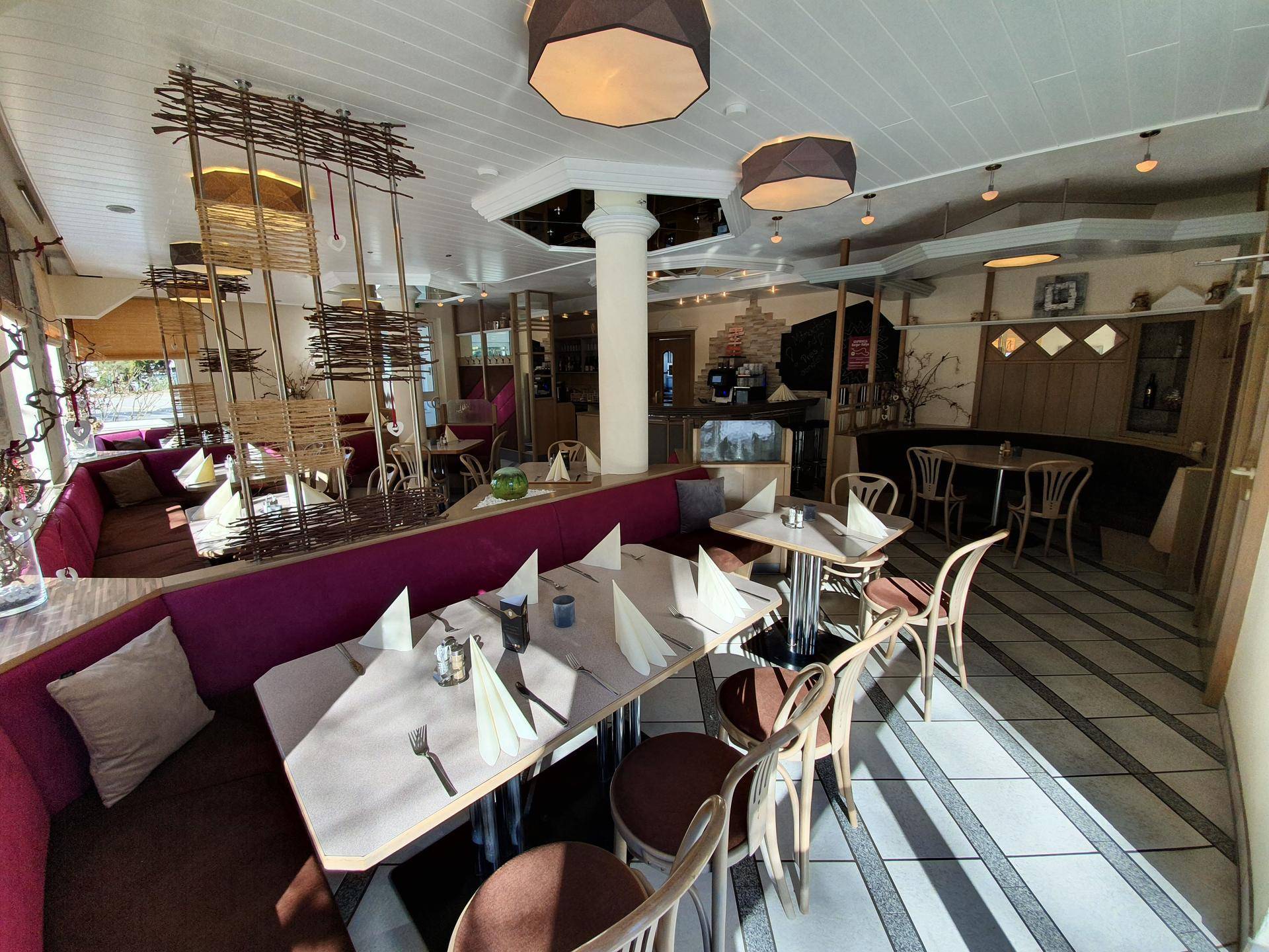 Gemütlicher Restaurantbereich mit gepolsterten Sitzbänken, Holztischen und dekorativer Beleuchtung.
