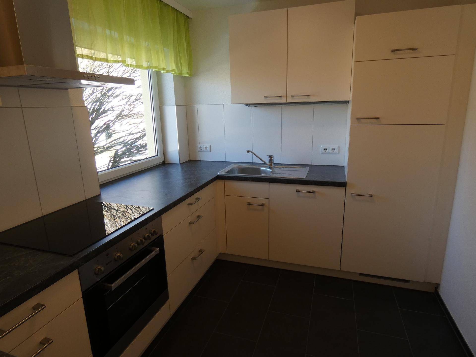 Moderne Einbauküche mit hellen Schränken, dunkler Arbeitsplatte und Induktionskochfeld.