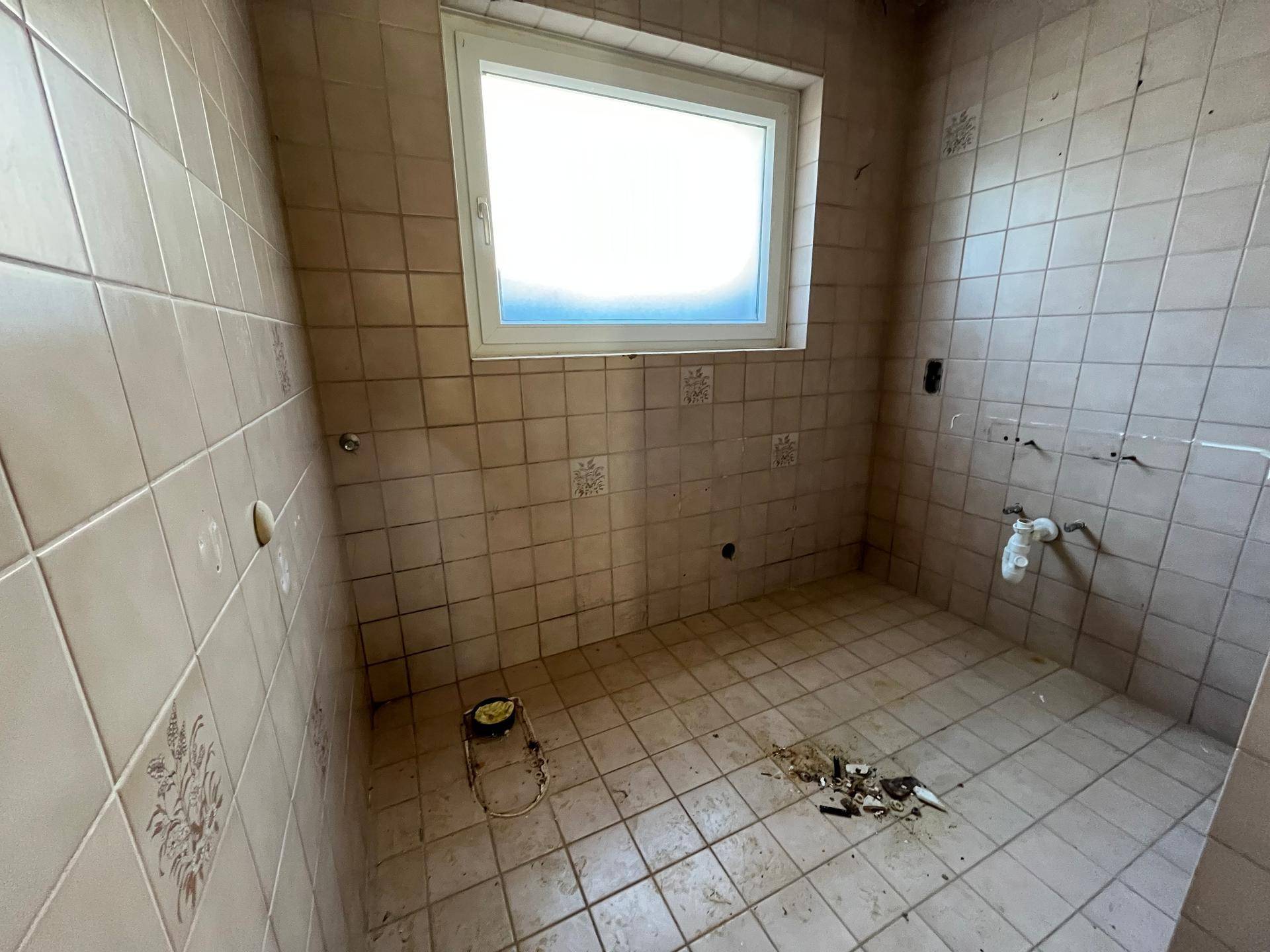 Badezimmer mit beigefarbenen Fliesen und Fenster, das eine vollständige Renovierung benötigt.