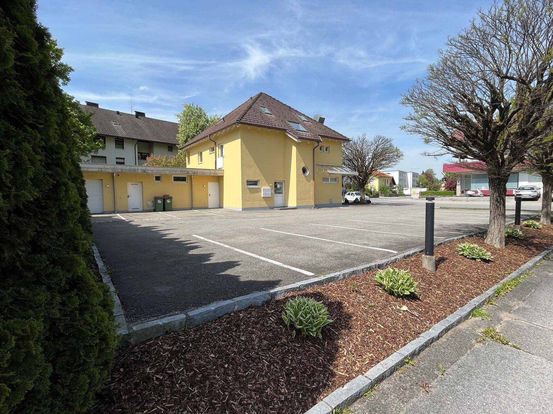Rückansicht des gelben Gebäudes mit großem Parkplatz und umliegenden Bäumen.