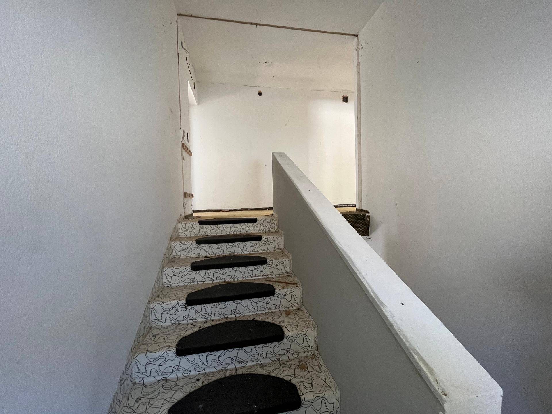 Treppenaufgang mit schlichtem Geländer und weiß gestrichenen Wänden, der in die obere Etage führt.