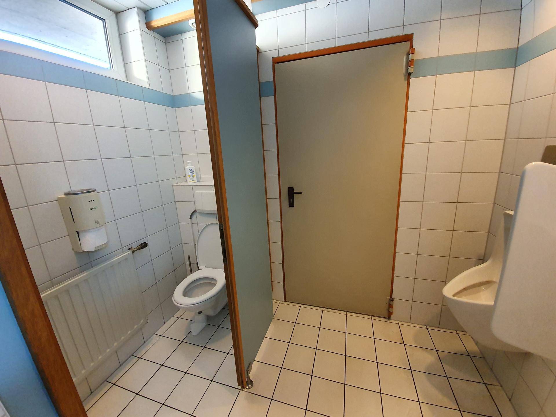 Helle Toilettenkabine mit WC, Urinal und Fliesenboden, gut gepflegt und funktional.