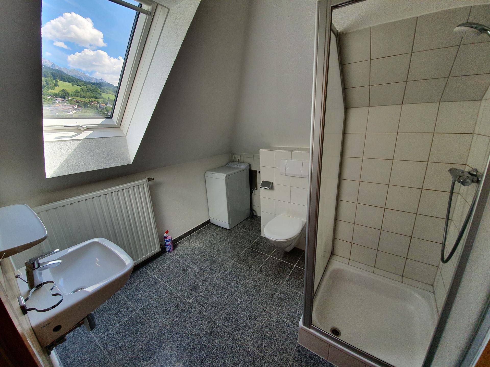 Badezimmer im Dachgeschoss mit Dusche, WC und Waschmaschine, hell durch Dachfenster.