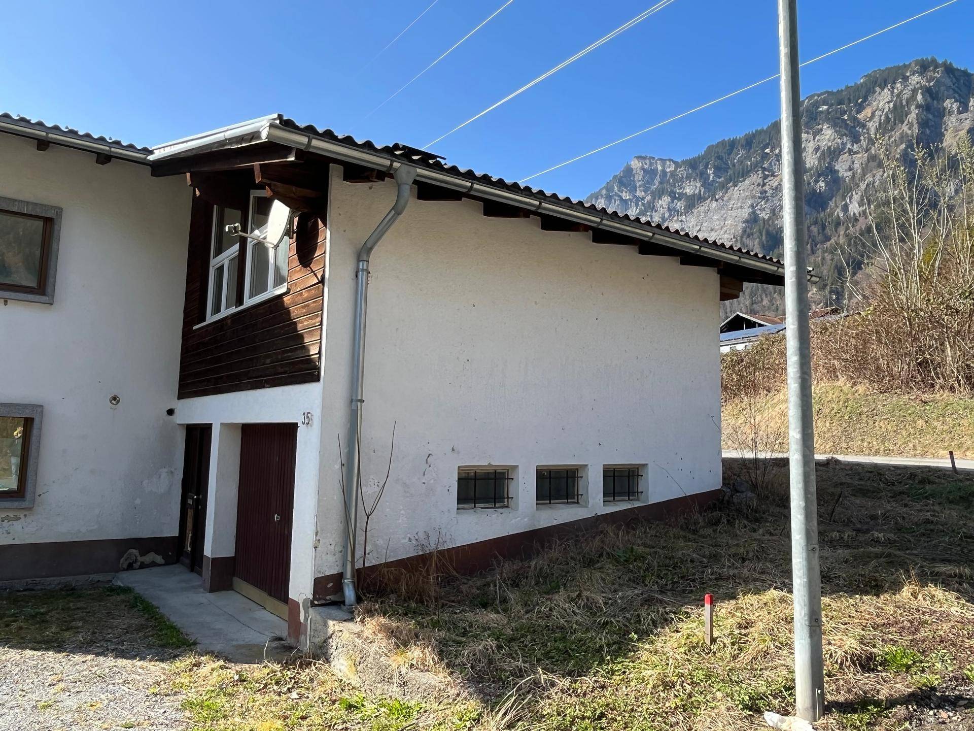 Seitenansicht des Hauses mit Garage und Fenstern, umgeben von natürlicher Landschaft.