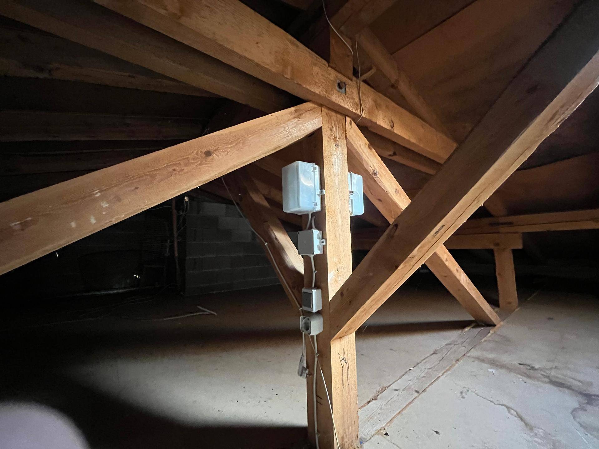 Unausgebauter Dachboden mit sichtbaren Holzbalken und einfacher Beleuchtung.