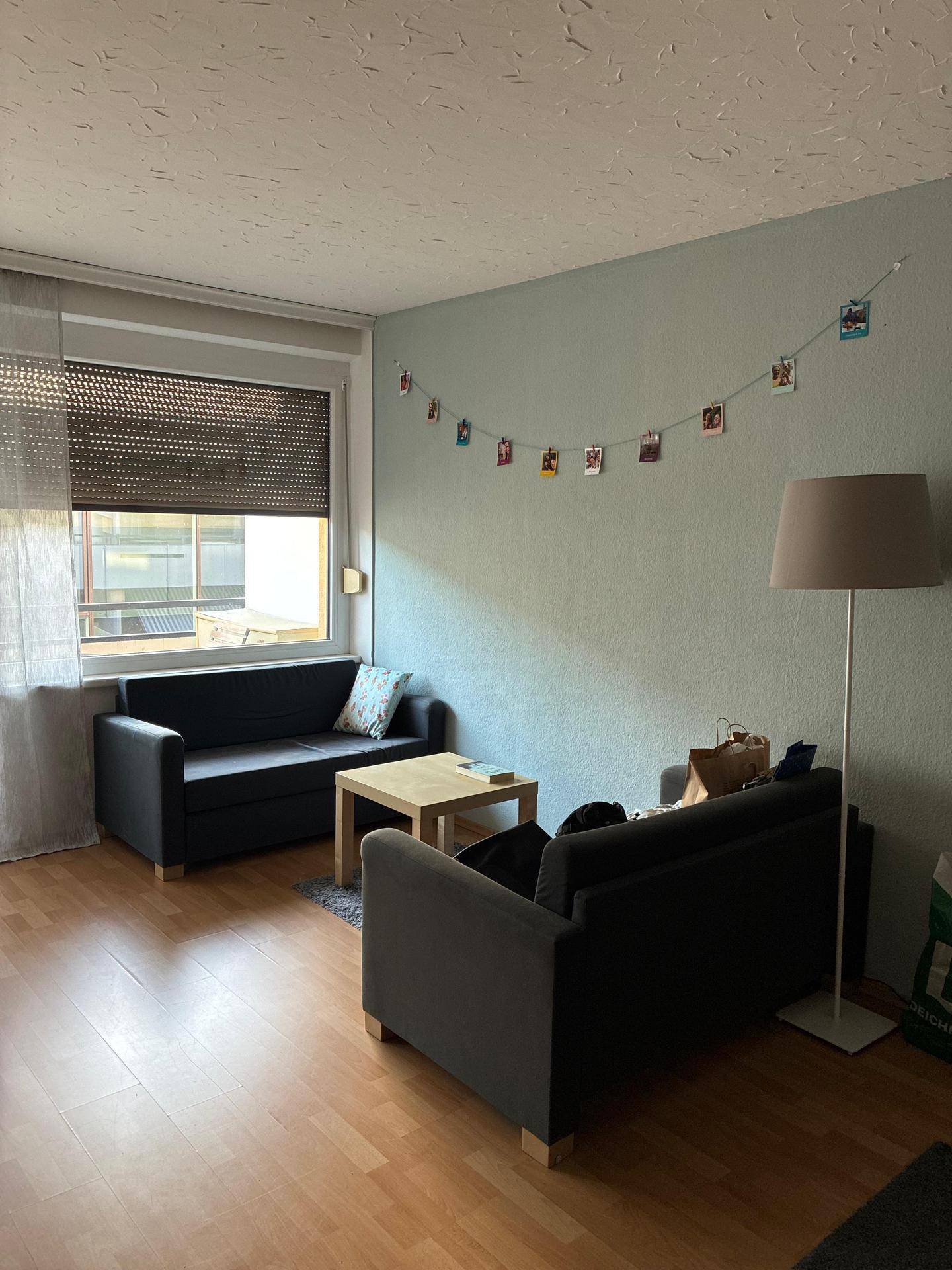 Gemütlicher Wohnbereich mit zwei dunklen Sofas, Couchtisch und Stehlampe, gut beleuchtet.