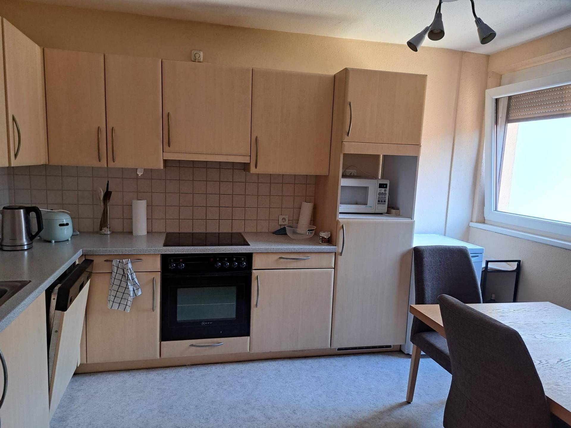 Funktionale Einbauküche mit hellen Holzfronten, Kochfeld, Backofen und Essbereich am Fenster.