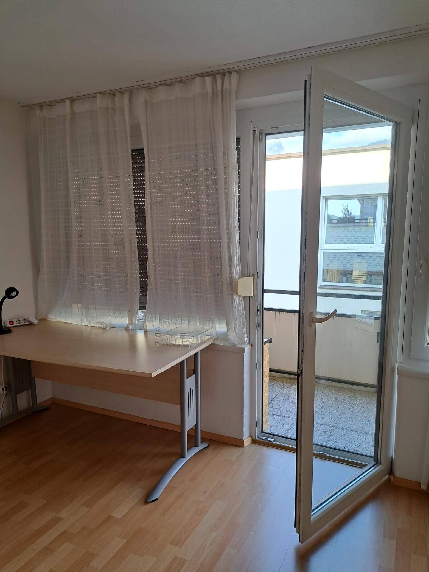 Heller Raum mit Schreibtisch, Holzfußboden und Zugang zu einem Balkon.