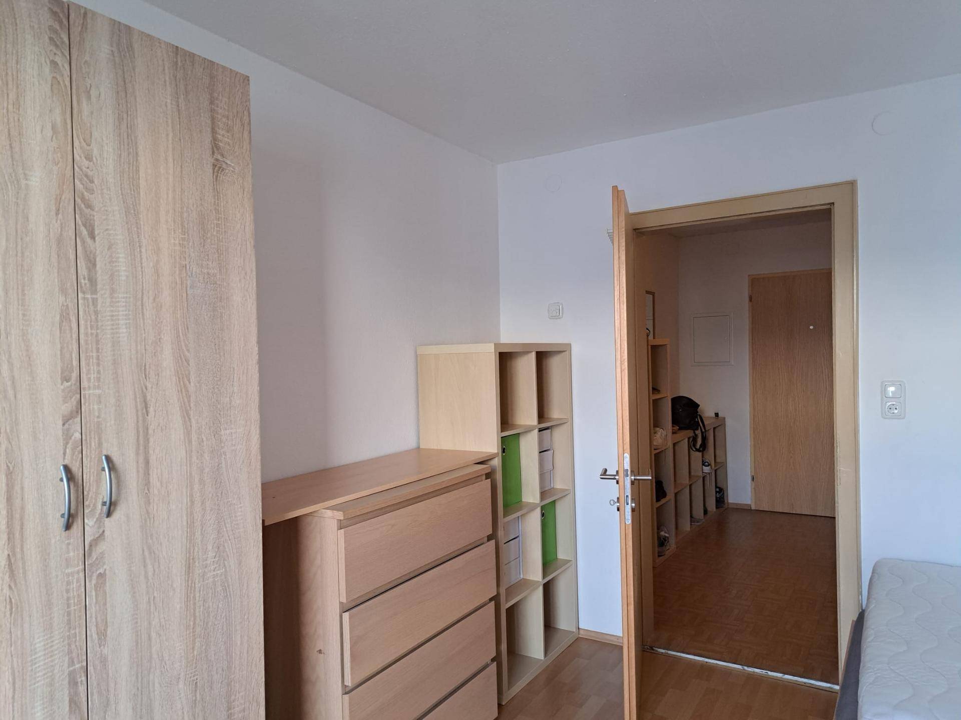 Schlafzimmer mit hellem Holzschrank, Kommode und Blick in den Flur.