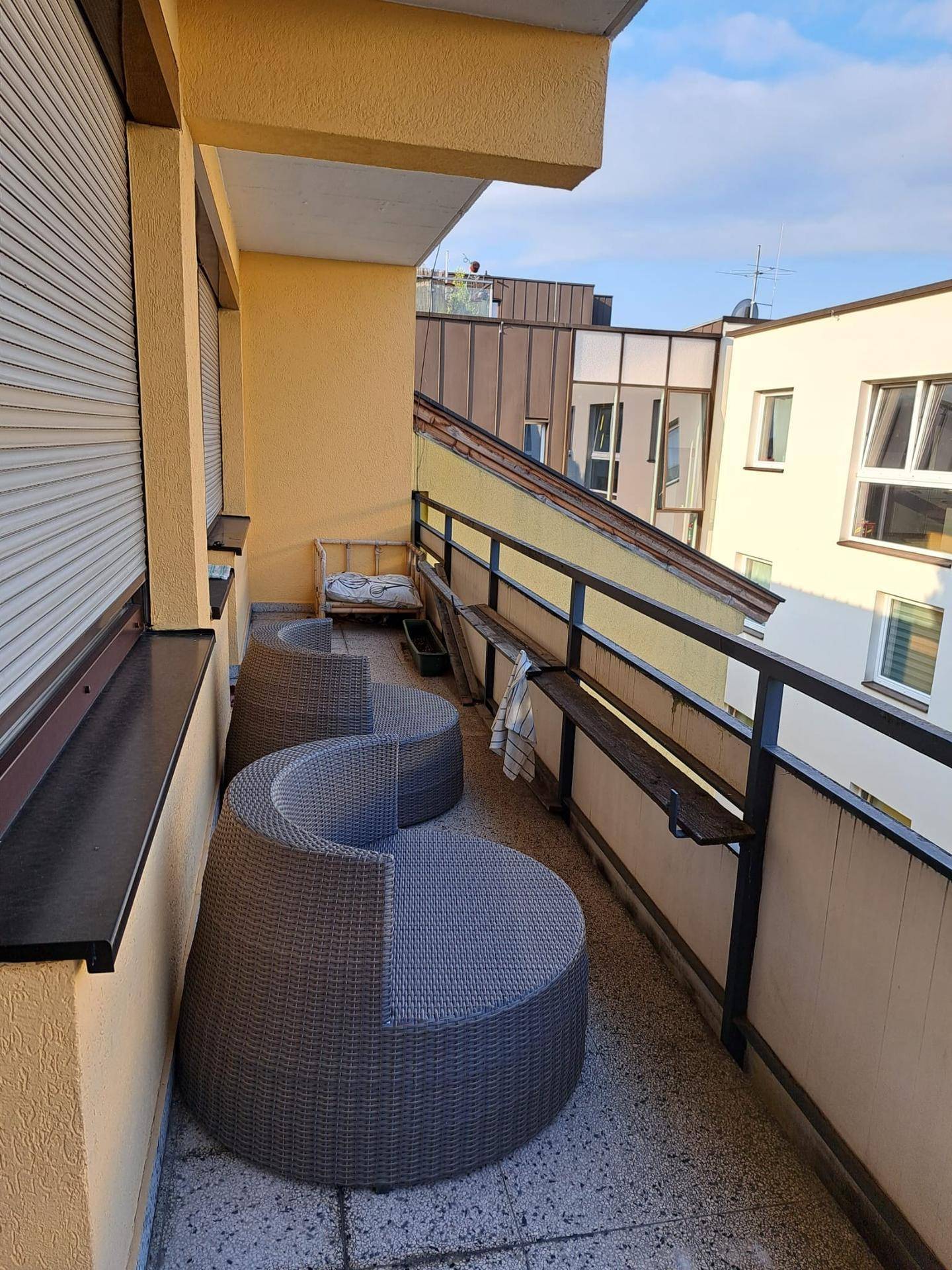 Schmaler Balkon mit zwei modernen Sitzgelegenheiten und Blick auf die umliegenden Gebäude.