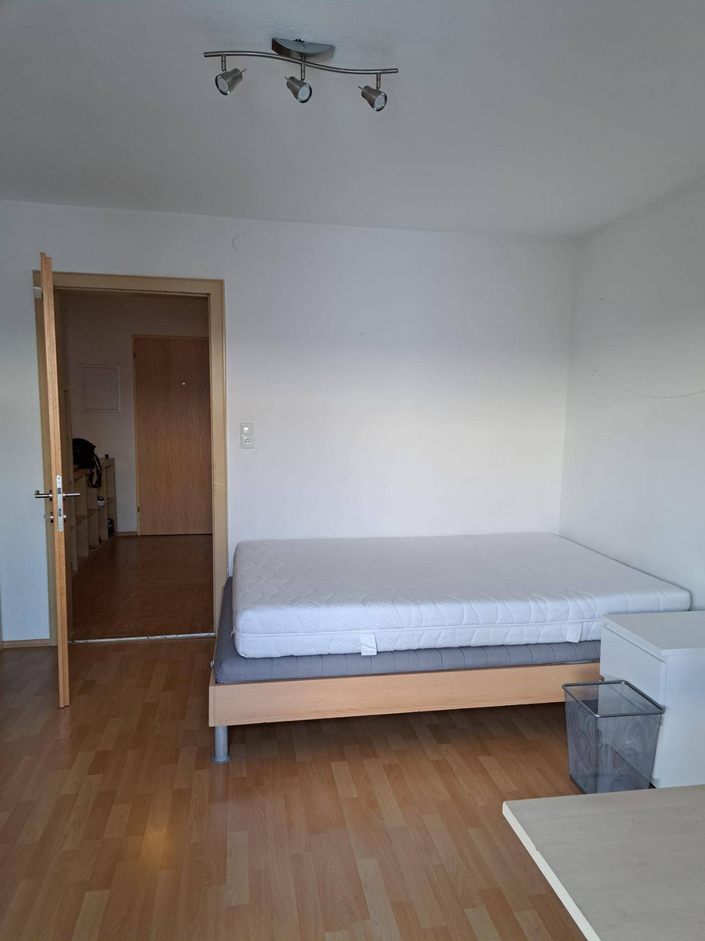 Schlafzimmer mit Bettgestell, Matratze und Zugang zu einem weiteren Raum.