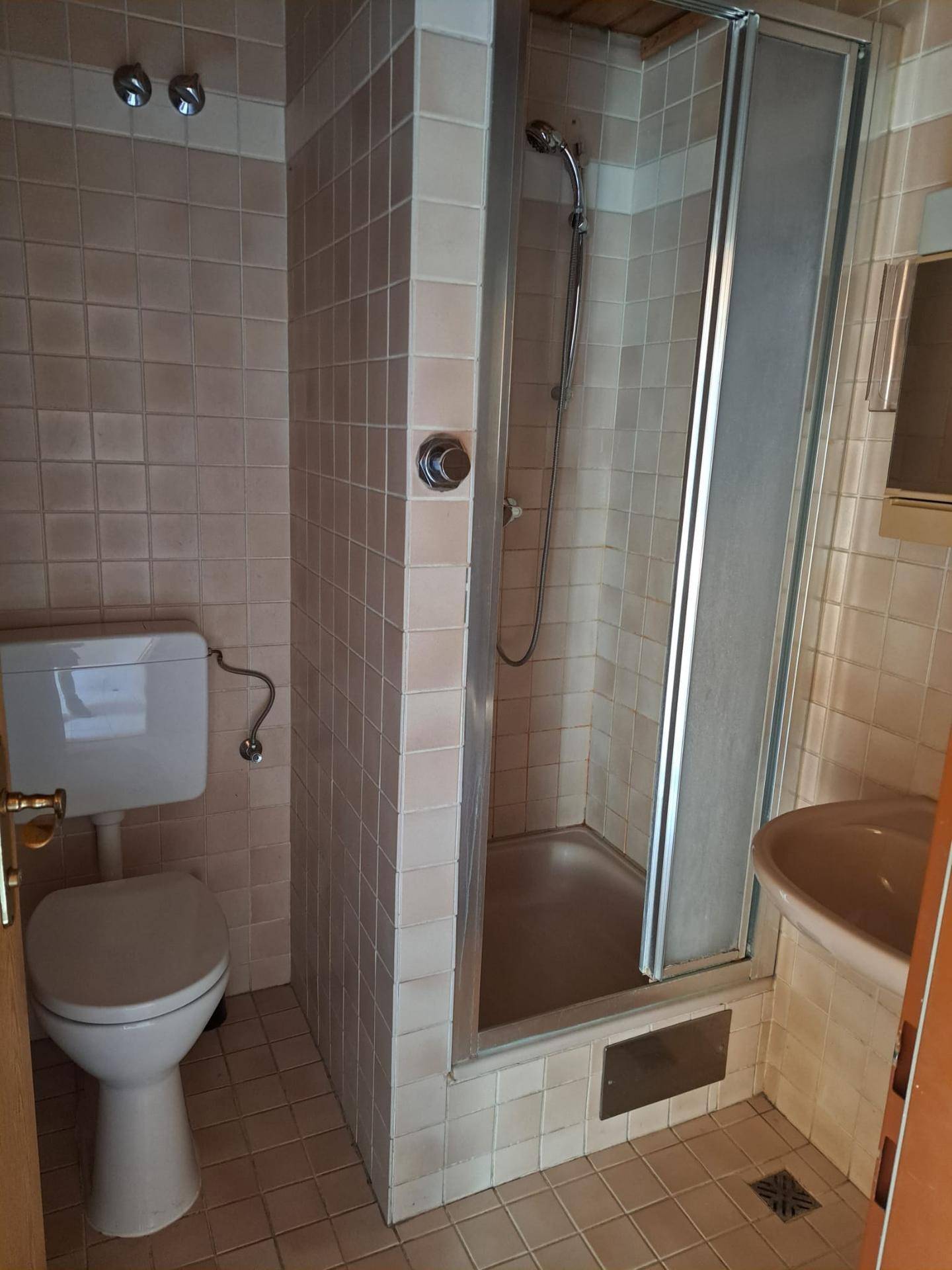 Badezimmer mit rosafarbenen Fliesen, Duschkabine, Toilette und kleinem Waschbecken.