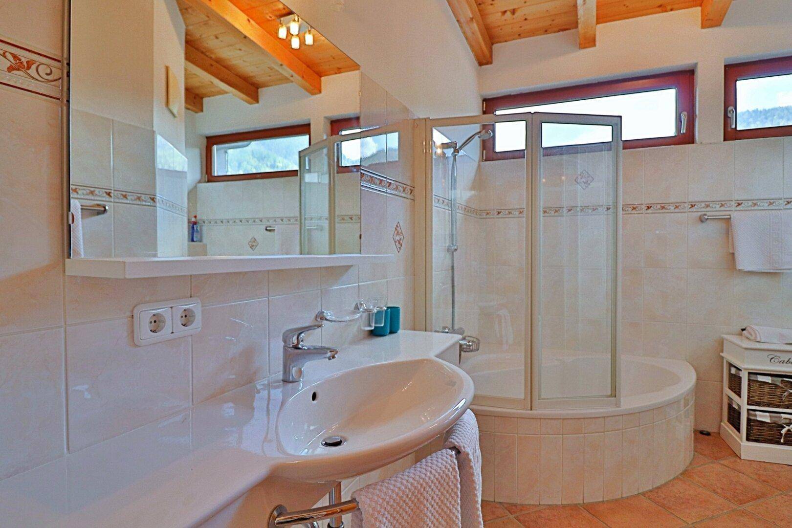 Gefliestes Badezimmer mit Dusche, Eckbadewanne und Fenster für Tageslicht.
